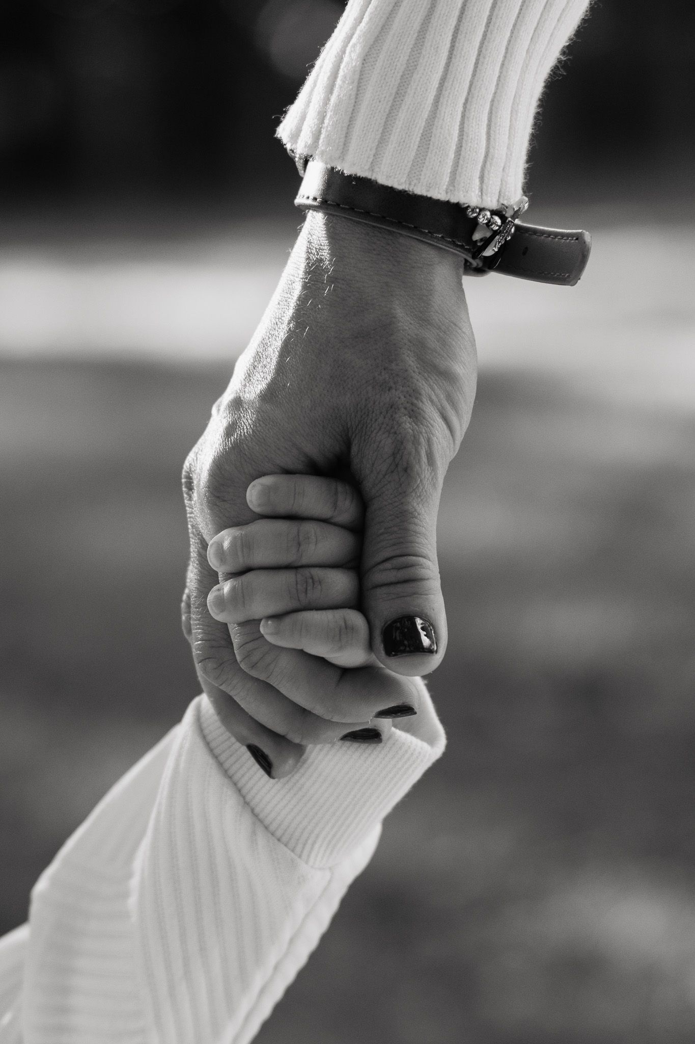 Black and white close-up photo of two hands holding each other in a loving gesture against a blurred background.