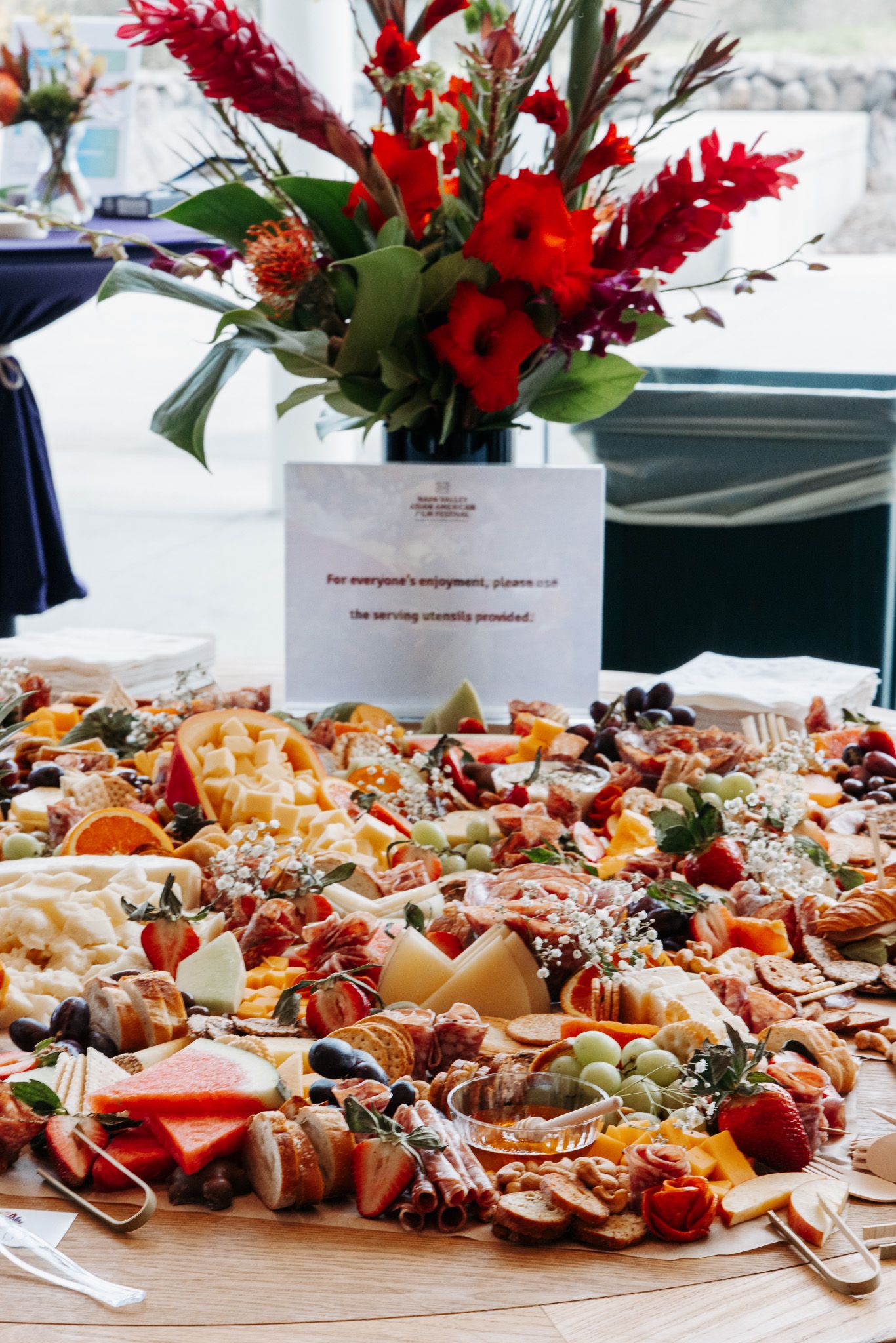 An elegant catering display with assorted appetizers and red floral centerpieces on a long table.