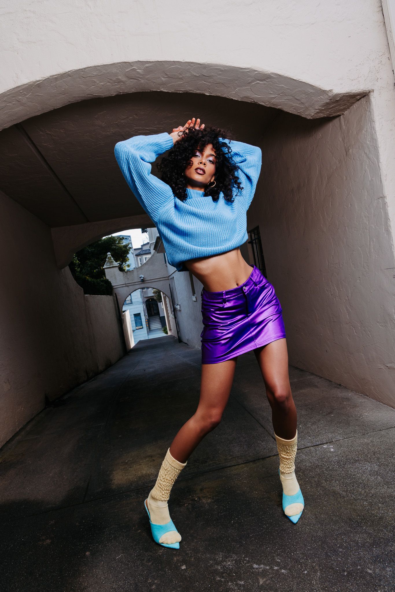 Dynamic dance poses in a concrete tunnel featuring blue sweater, purple skirt and turquoise heels.