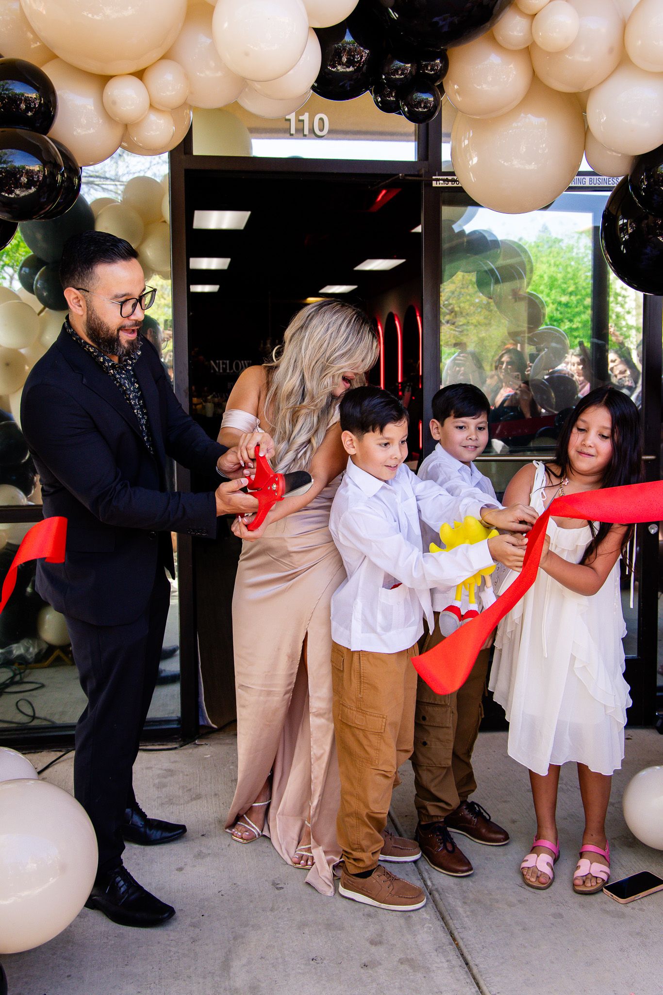 A group participates in a ribbon cutting ceremony with balloon decorations at a business grand opening event.