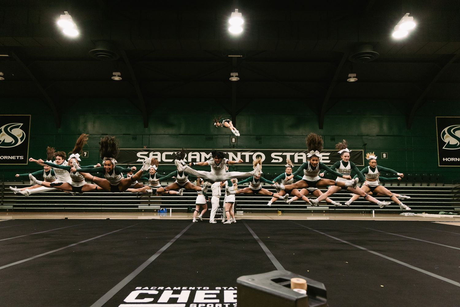 Sacramento State cheer team performs synchronized jumps on indoor practice mat.