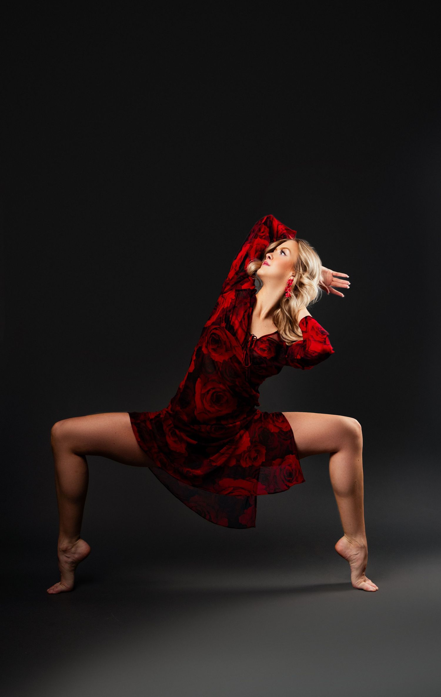 Dancer in flowing red velvet dress performs dramatic pose against dark background, showcasing graceful movement and form.