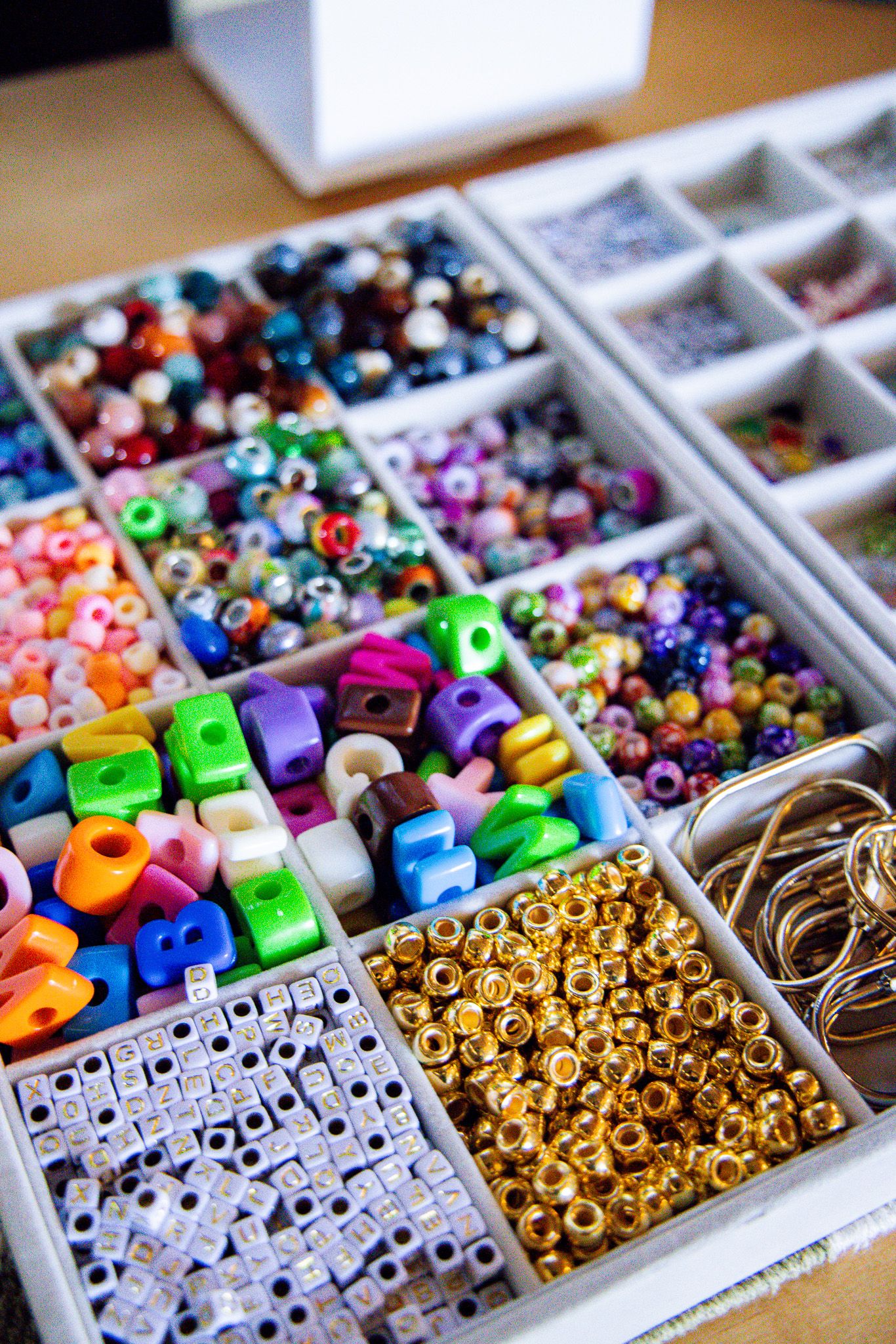 Colorful assorted craft beads organized in white compartment box including alphabet, gold, and mixed beads.