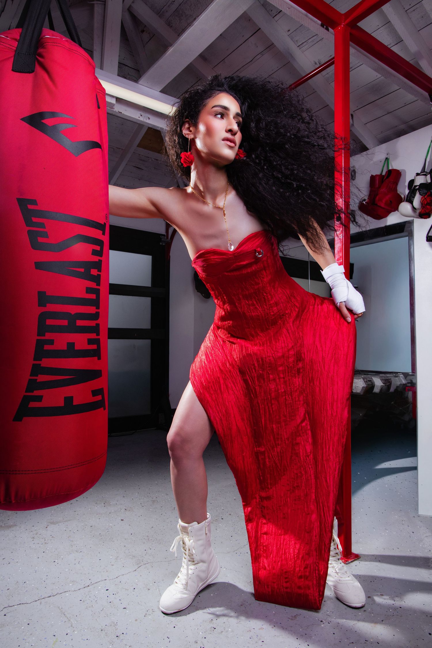 Woman in red strapless gown and white boxing gloves poses next to Everlast punching bag in a gym.