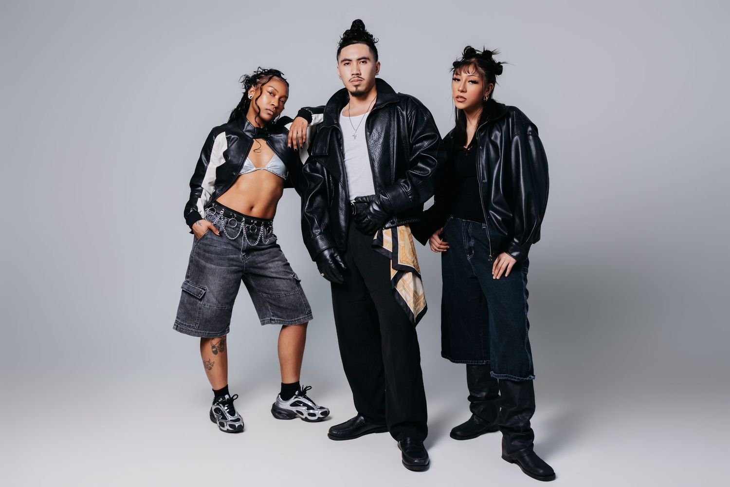 Three people in black outfits strike dynamic poses against a white studio backdrop for a fashion photoshoot.