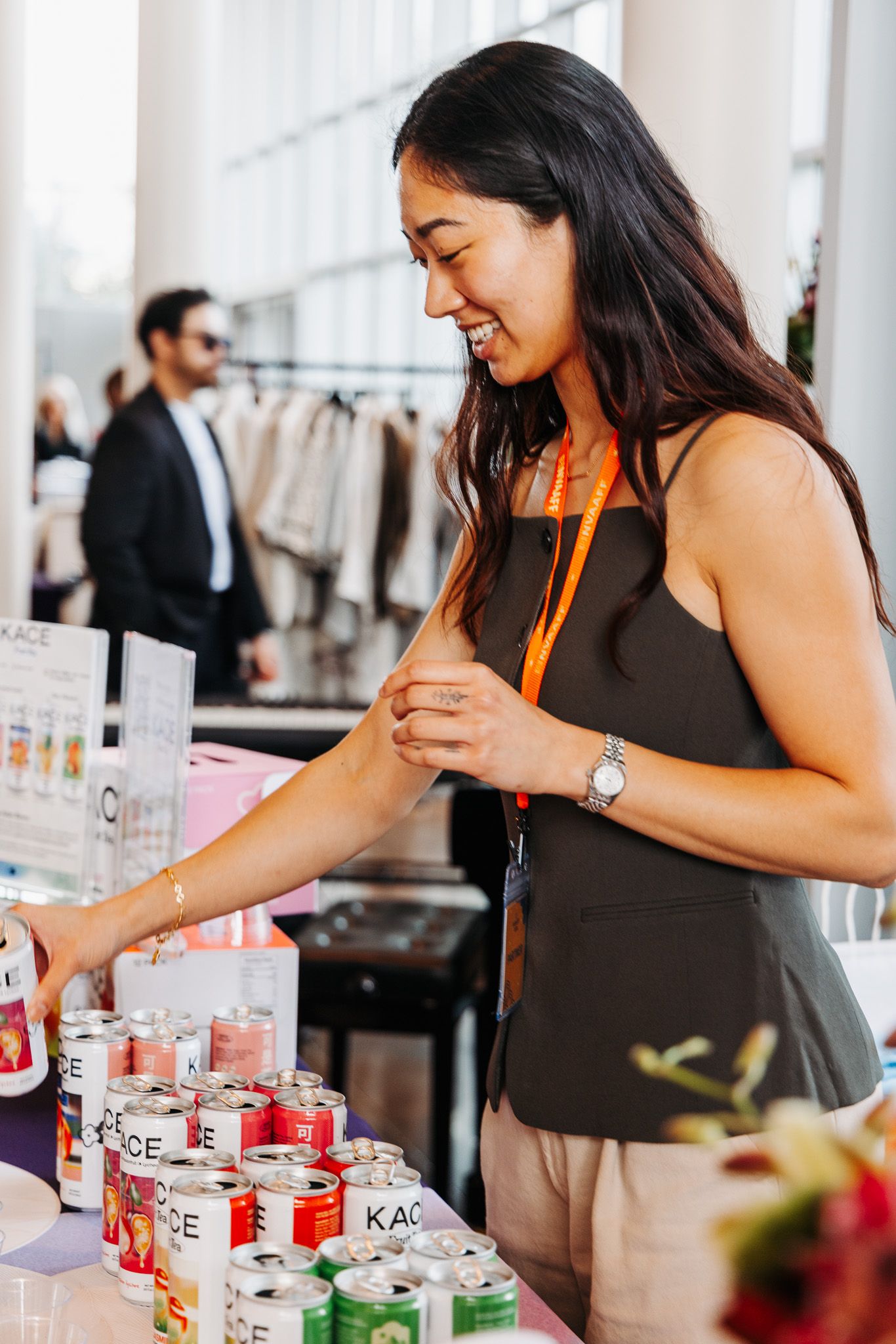 A smiling woman in a black sleeveless top browses colorful canned beverages at a retail display.
