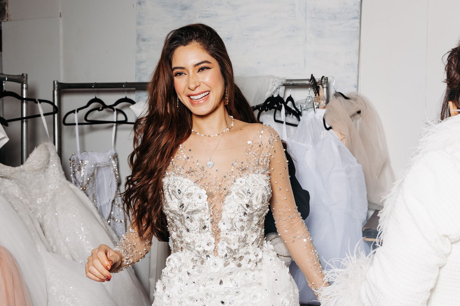 Model in crystal-embellished sheer wedding dress smiling during fitting in bridal boutique.