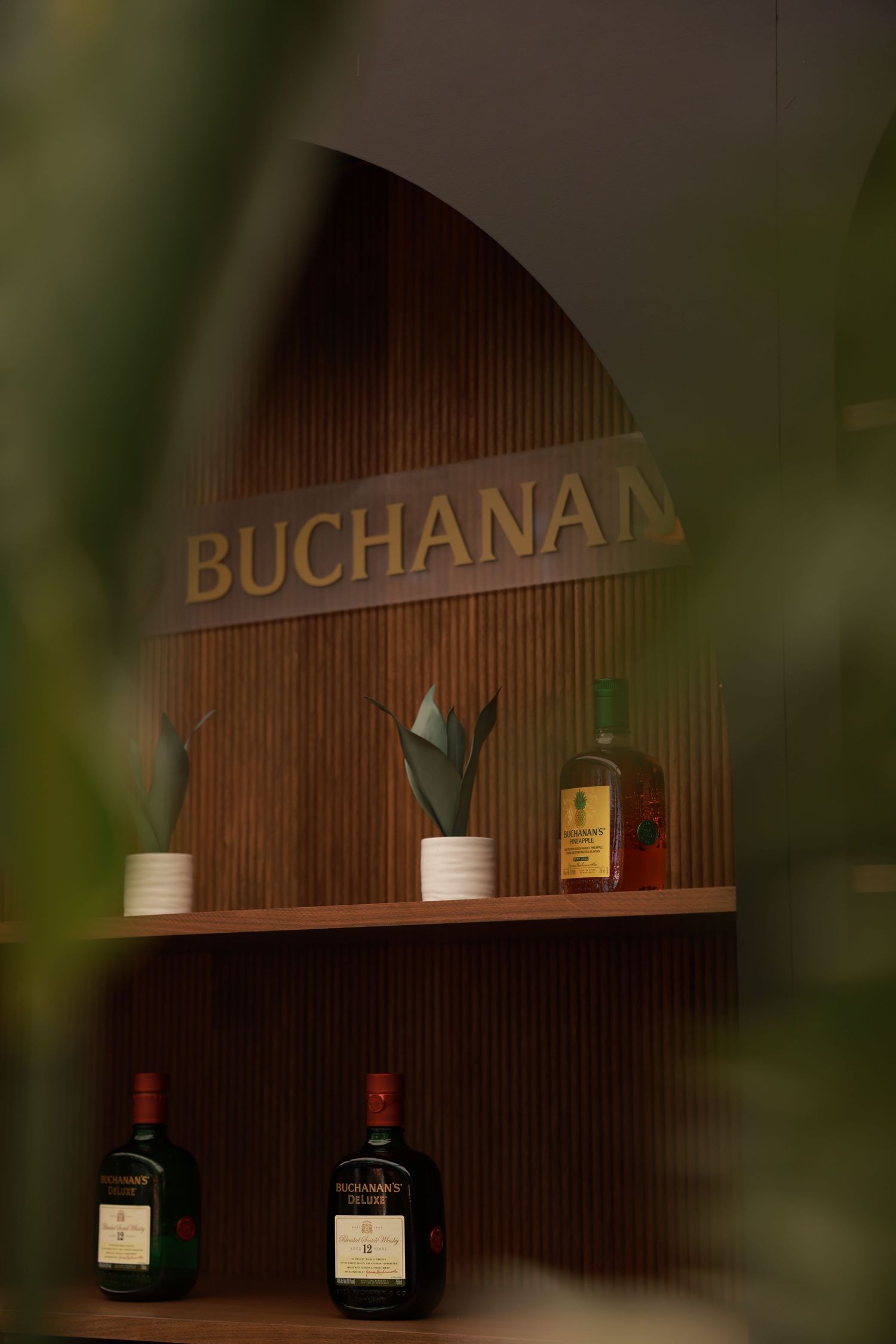 Wooden bar display with Buchanan's whiskey bottles and signage in dim lighting.