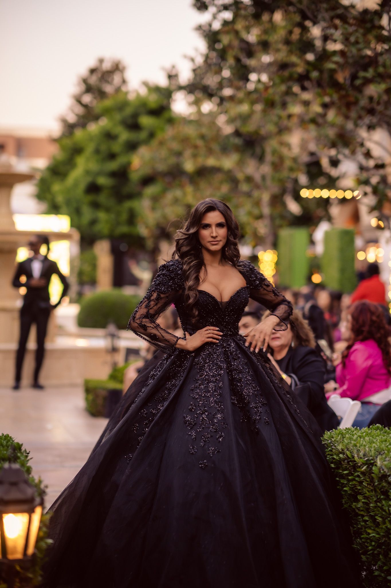 A dramatic black evening gown with a full tulle skirt photographed at dusk in an outdoor garden setting.