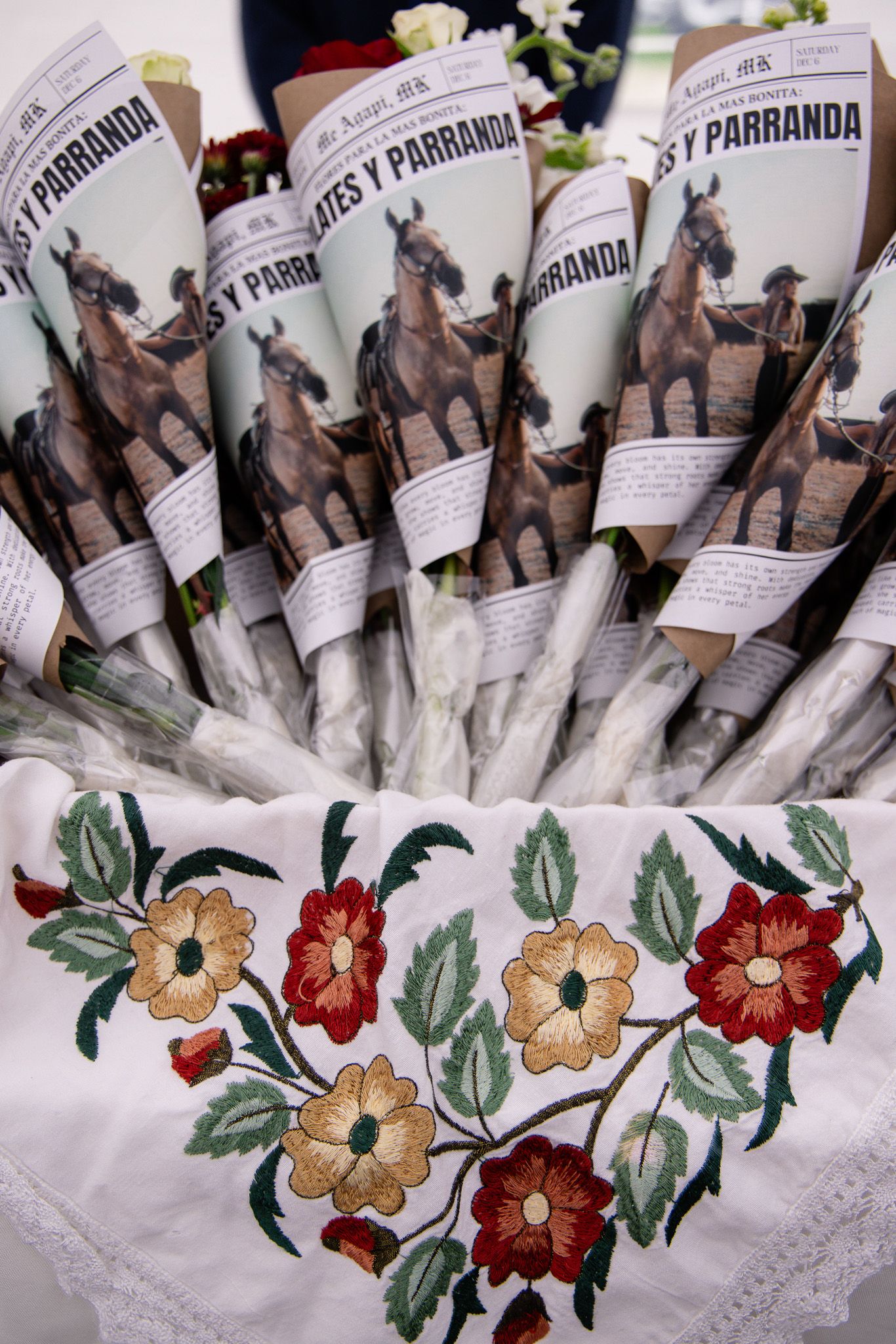 Row of wine bottles with decorative floral embroidered tablecloth featuring red and gold flowers.