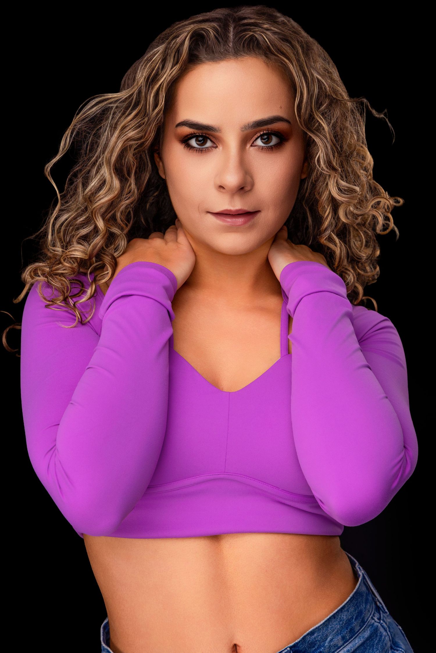 Studio portrait with vibrant purple crop top and curly hair against dark background.