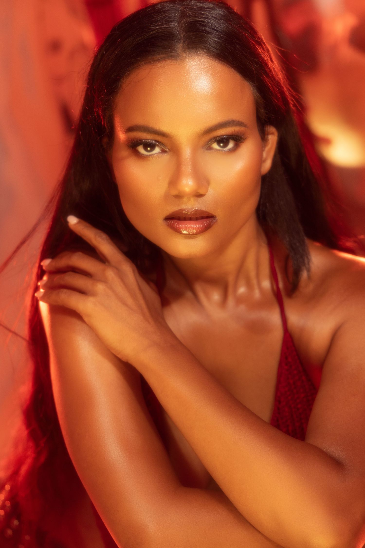 A glamour beauty portrait with dramatic red lighting and warm tones creating a sultry, artistic mood.
