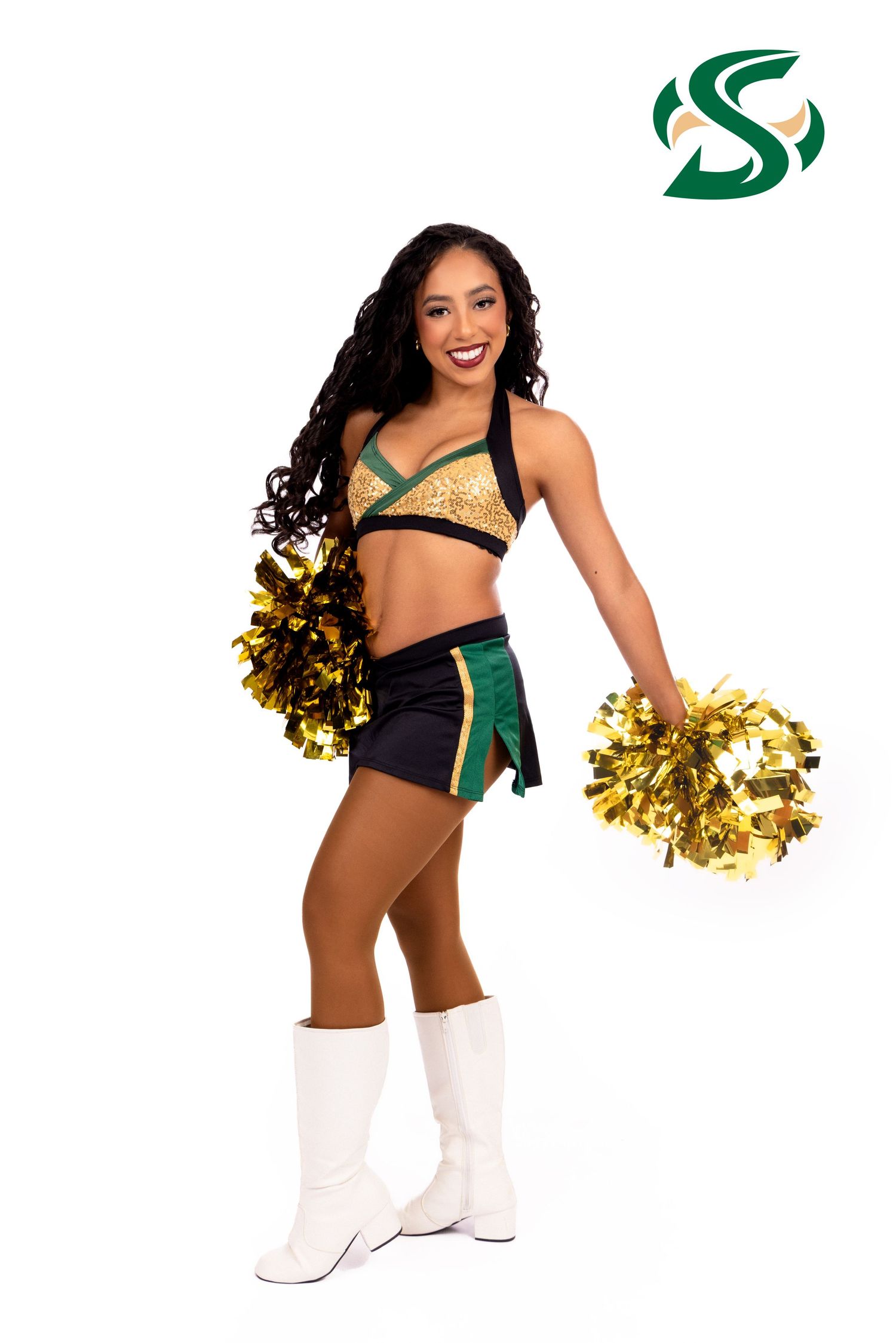 Professional cheerleader in green and black uniform with gold pom poms performing choreographed dance moves at sports event.