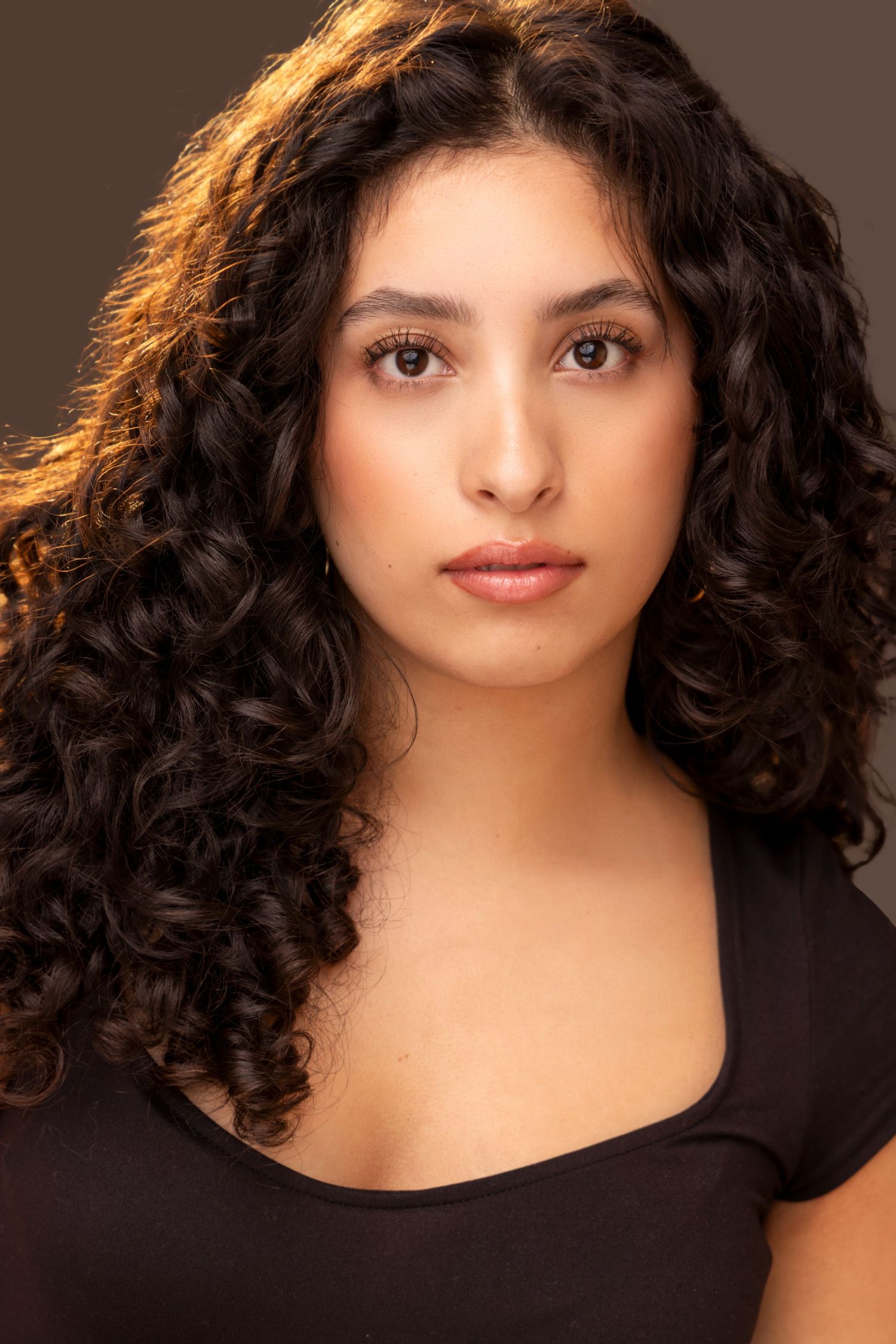 Portrait featuring dark curly hair and a black top against a dark background.