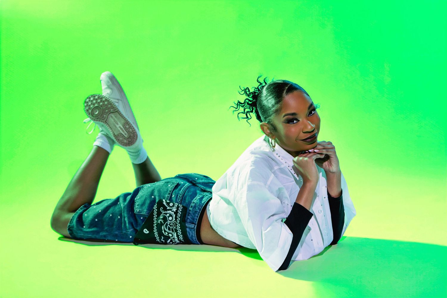 Young woman in white hoodie and green cargo pants poses on a vibrant green background in white sneakers.