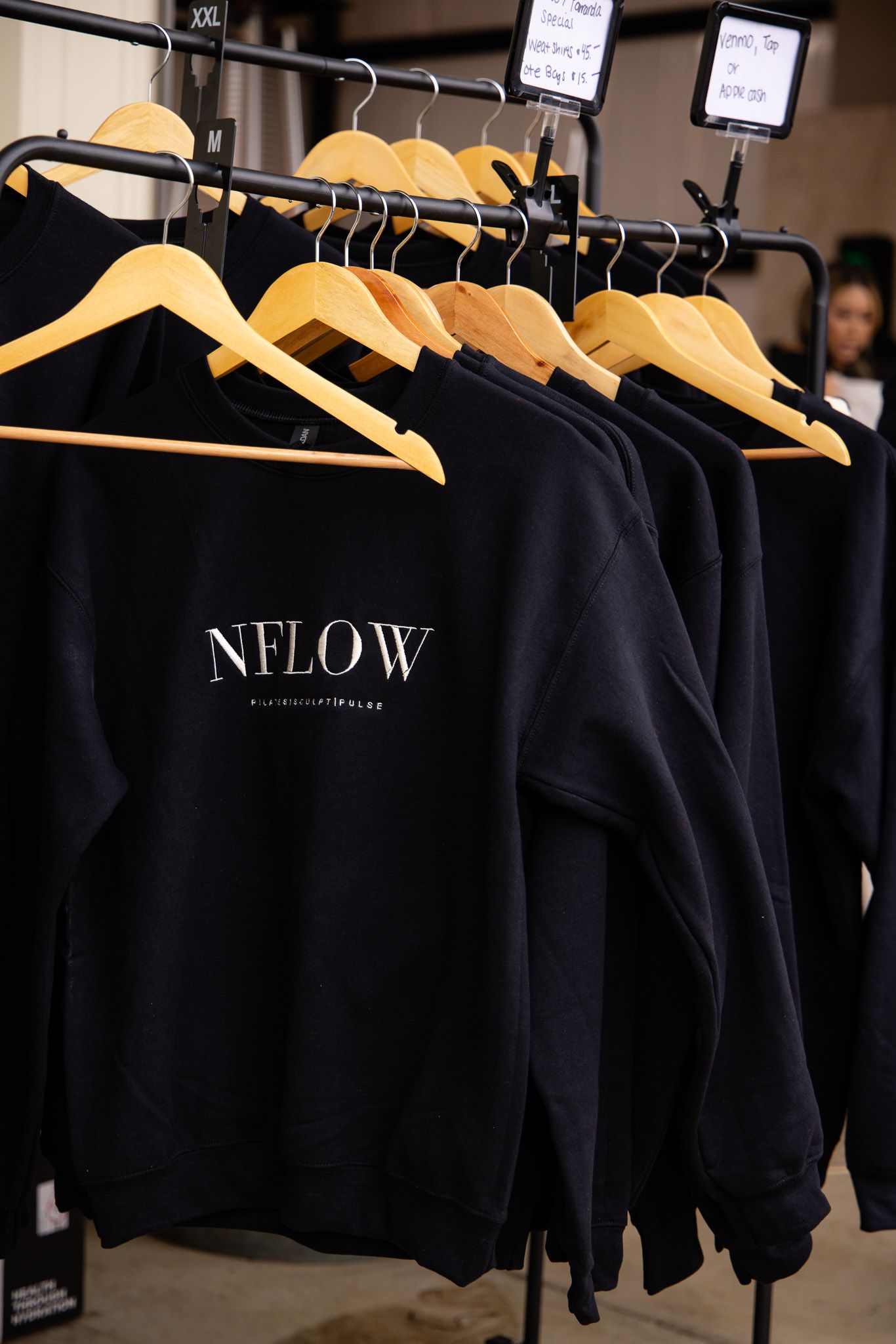 Black sweatshirts hanging on wooden hangers with NFLOW branding displayed in a retail setting.