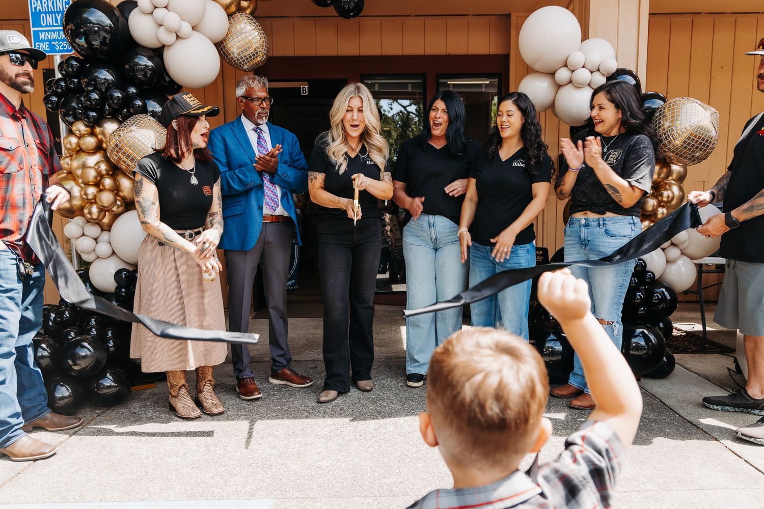 Ribbon cutting ceremony with group of people in front of balloon arch decorations at grand opening event.