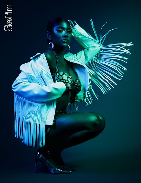 Artistic fashion photo with model wearing white fringe costume under ethereal turquoise lighting.