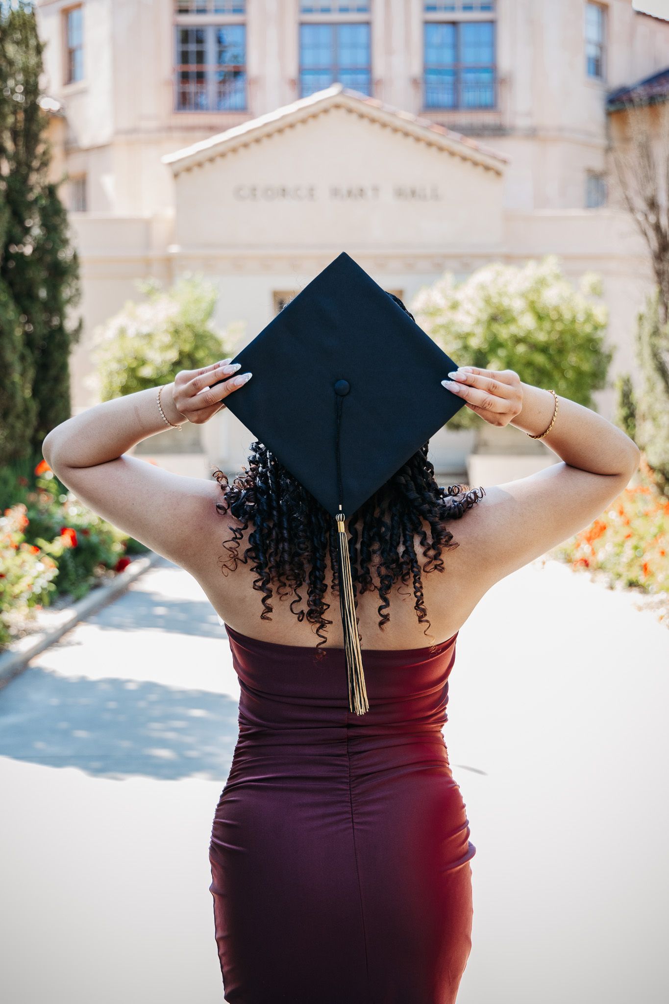 A graduation portrait series showing a dark graduation cap against a burgundy dress with architectural elements in the background.