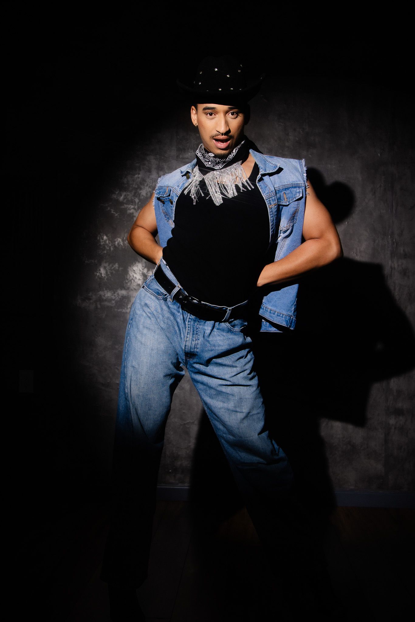 Dramatic black and white portrait series showing person in denim overalls and sleeveless shirt against dark background.