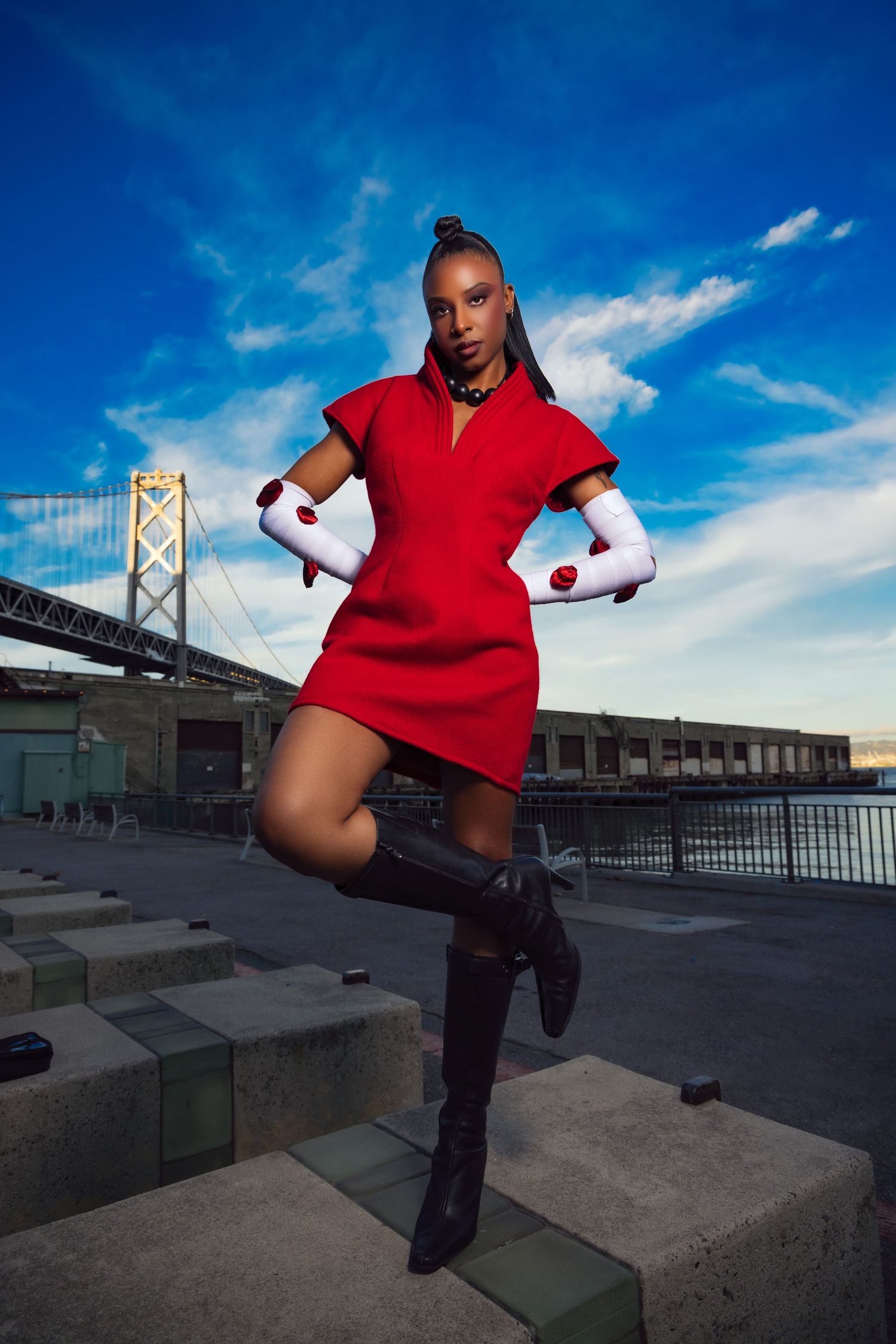 Dancer in red top performs dynamic moves against urban waterfront backdrop with bridge in background.