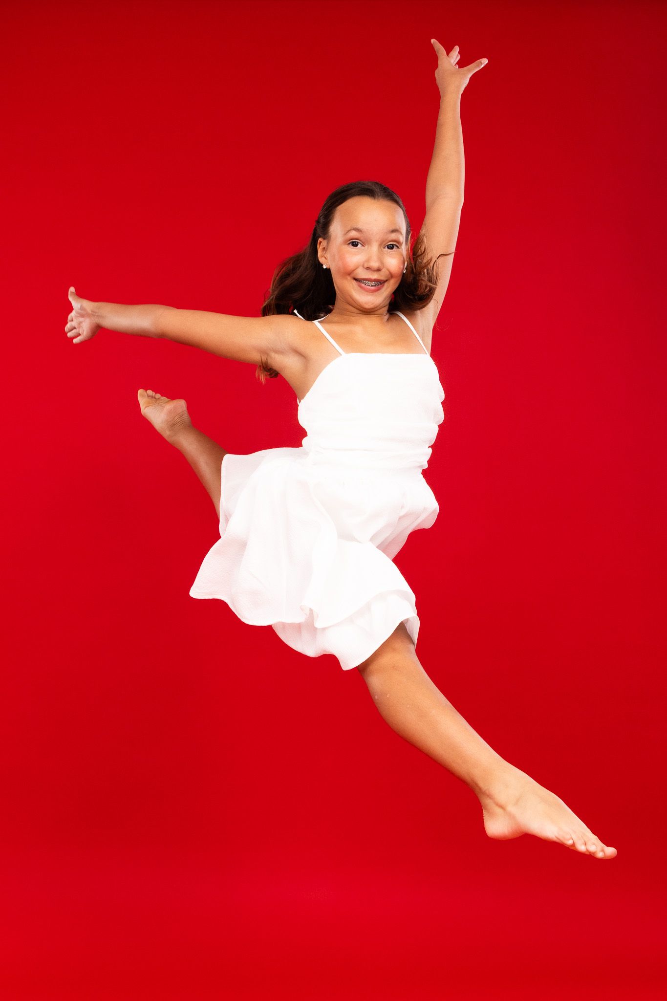 Energetic dance sequence captured in white dress against bold red studio backdrop.