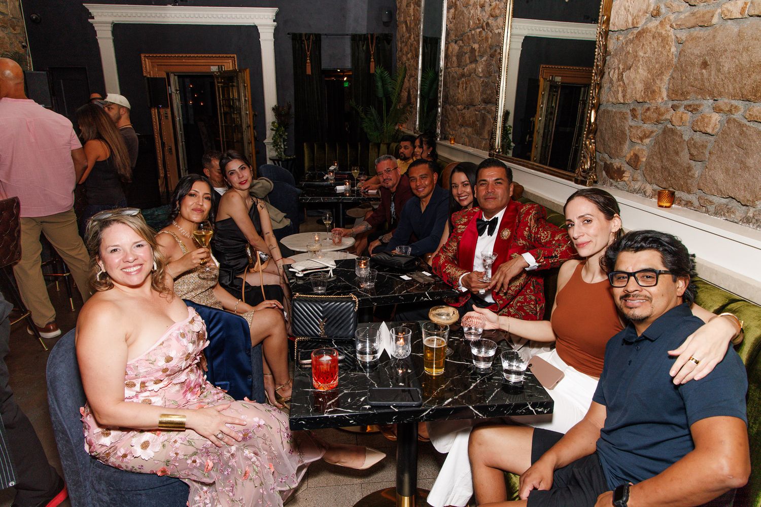 Group of elegantly dressed friends gathered around a table at an upscale restaurant or bar for a special occasion.