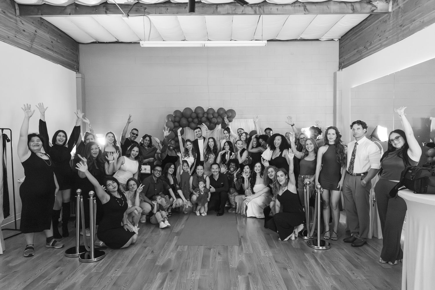 Large group of people posing together in a modern event space, celebrating with raised hands in black and white photo.