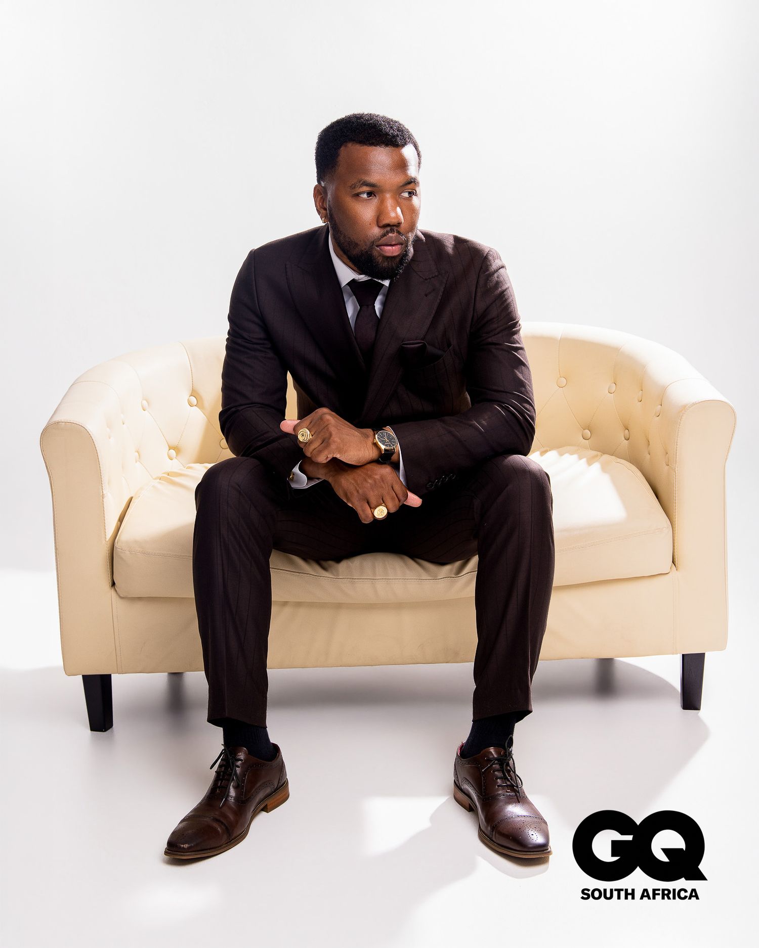 Man in dark suit sitting on cream sofa in GQ South Africa fashion editorial shoot.