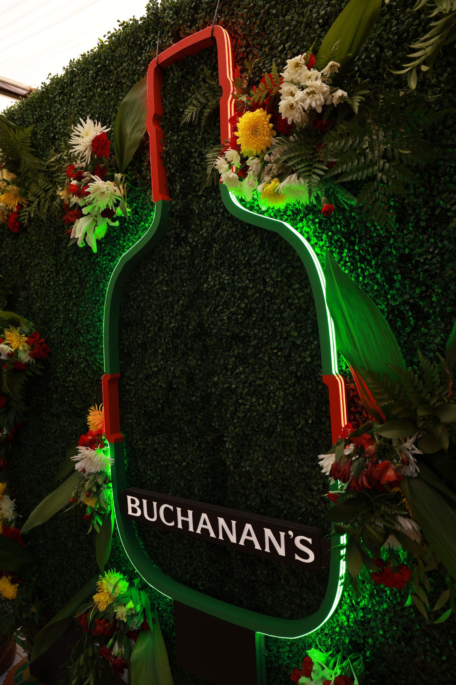 Illuminated green neon Buchanan's sign with floral decorations against dark background.