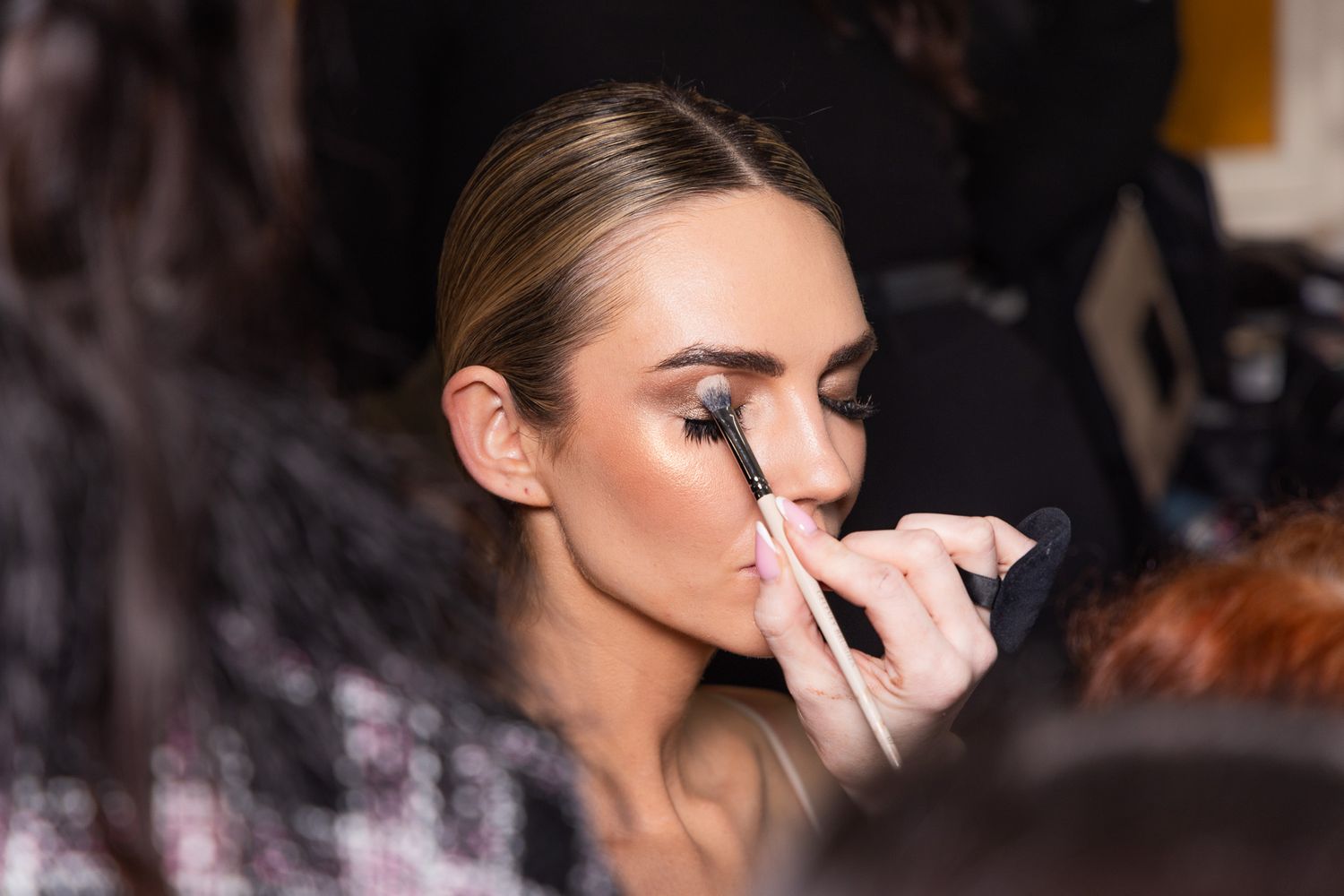 Behind-the-scenes makeup application shots in dark lighting showing cosmetic brushes at work.