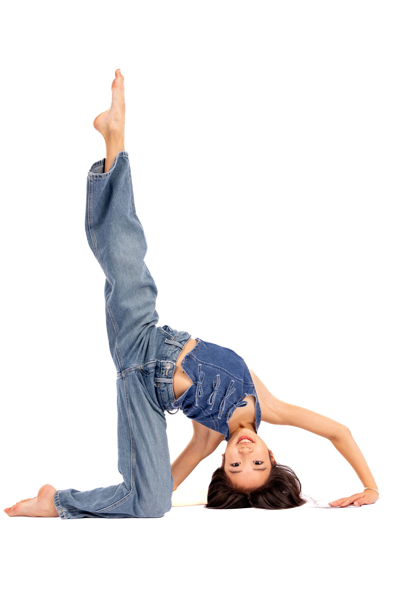 Flexible dancer in denim jeans performs a backbend pose with one leg raised on white background.