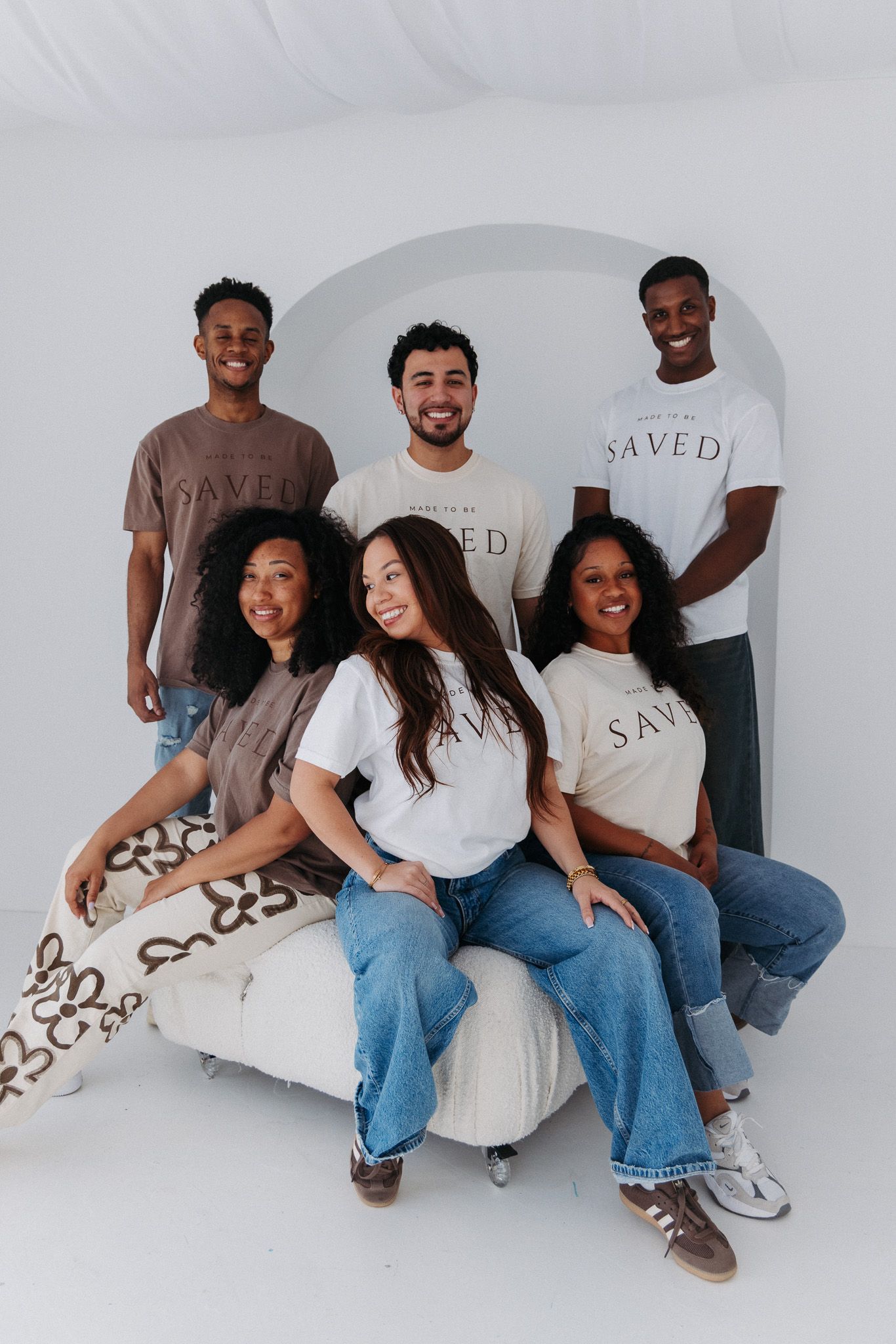 Happy friends in casual outfits sitting together against a white wall with SAVED text visible.