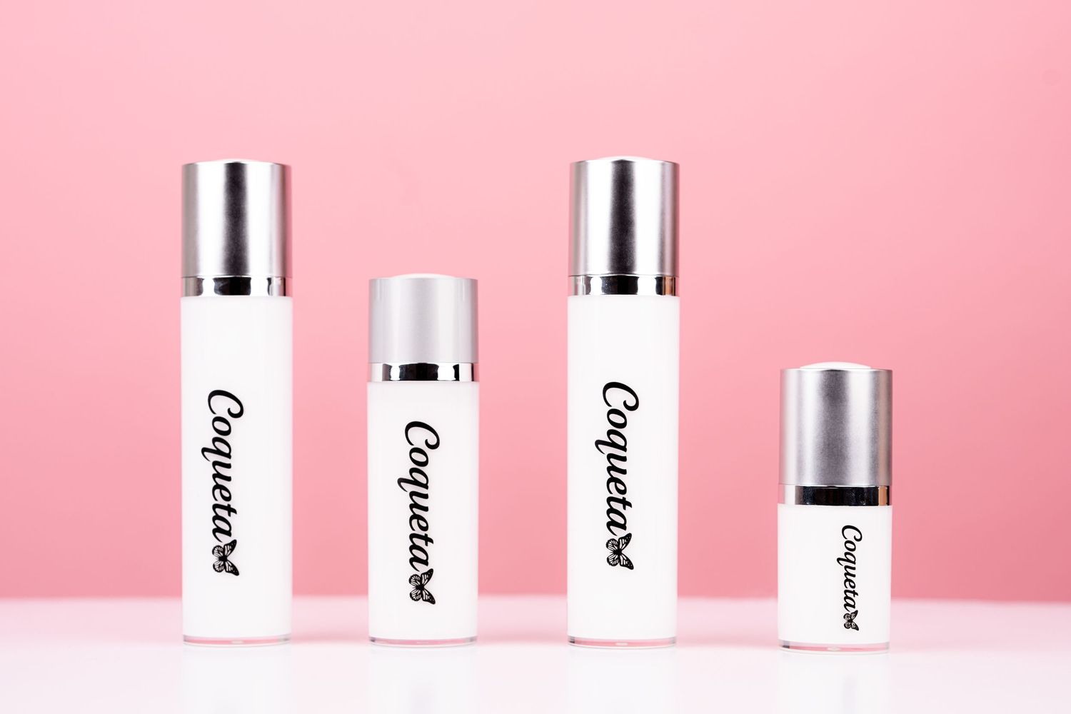 Beauty and skincare products arranged in white bottles against a soft pink background in minimal style.