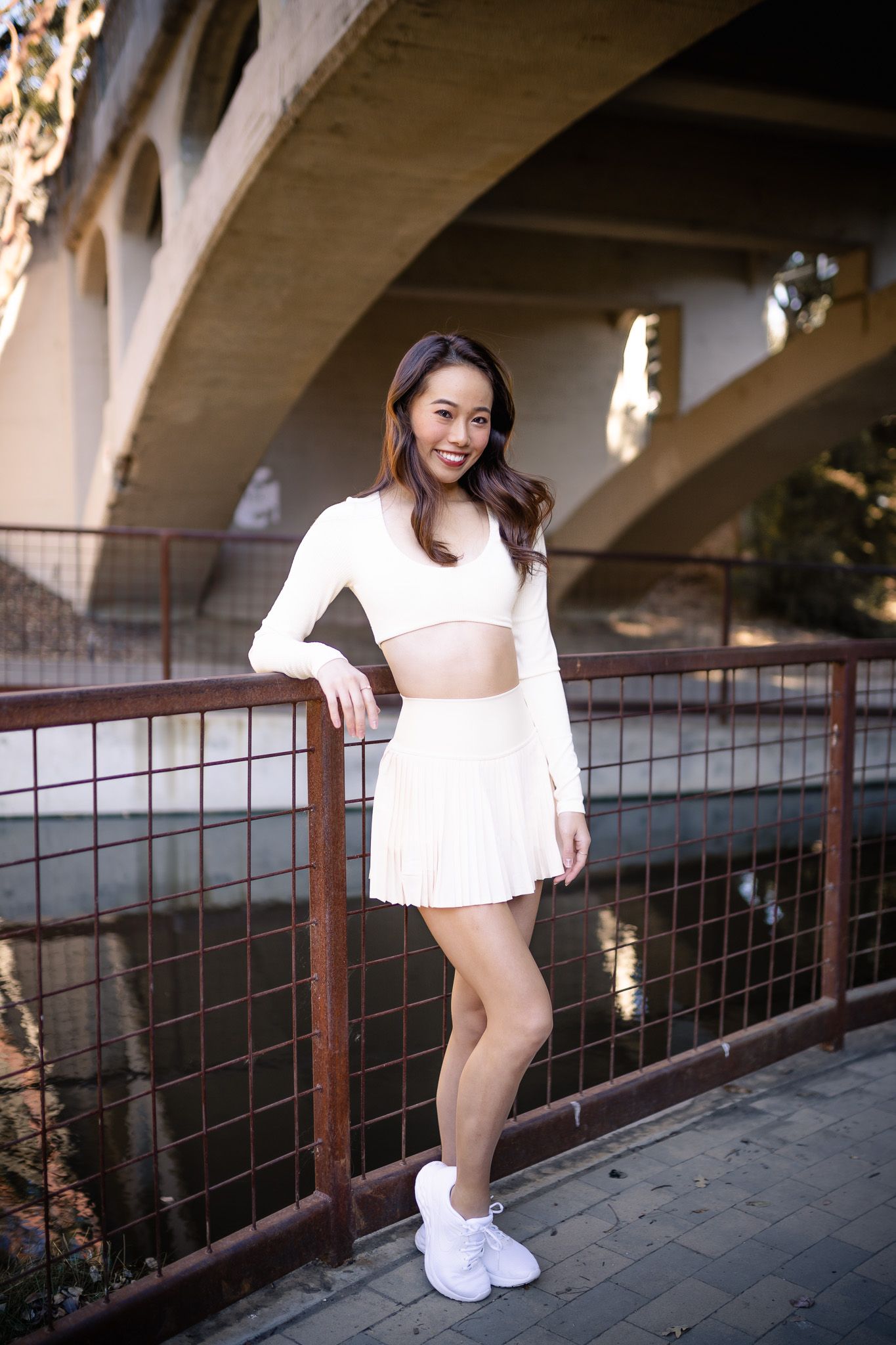 A person in a white dress leans against a metal railing under a bridge or overpass structure.