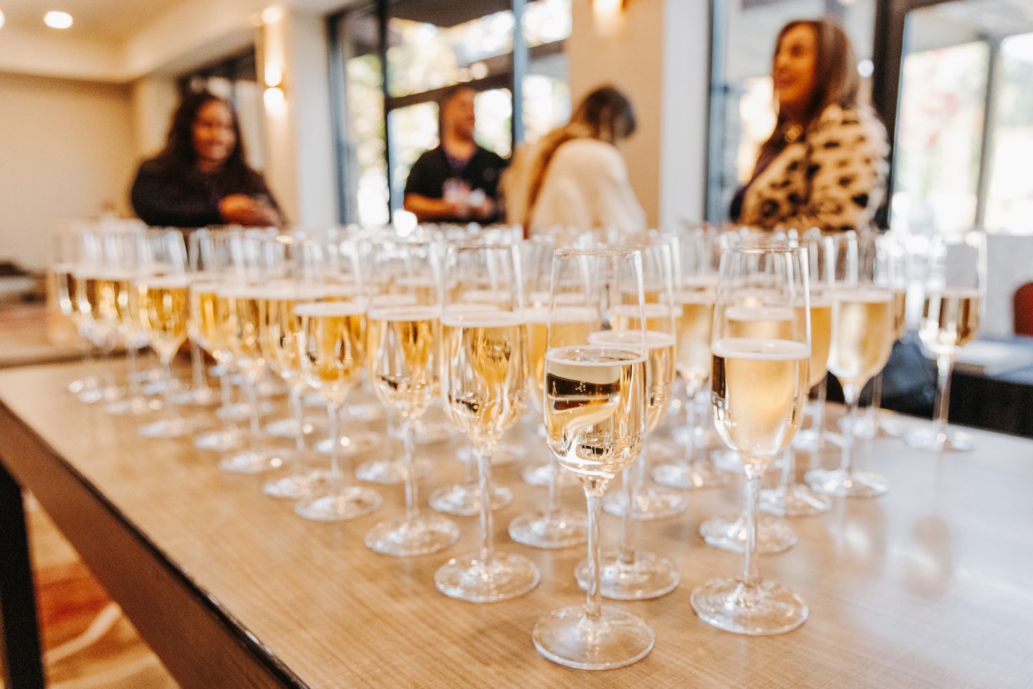 Multiple champagne glasses filled with sparkling wine arranged on a wooden table at a tasting event.