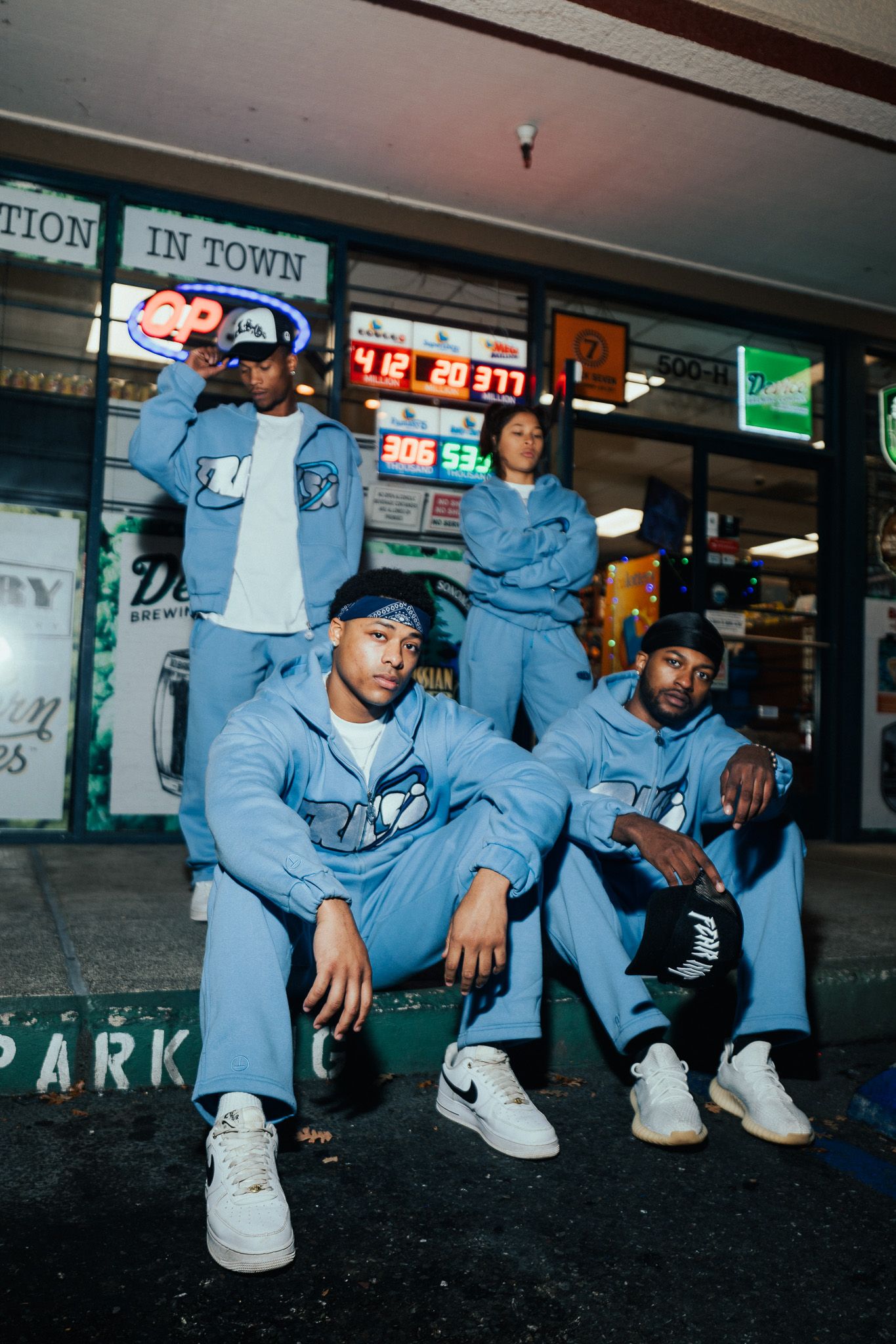 Four people in matching light blue tracksuits posing outside a convenience store at night.