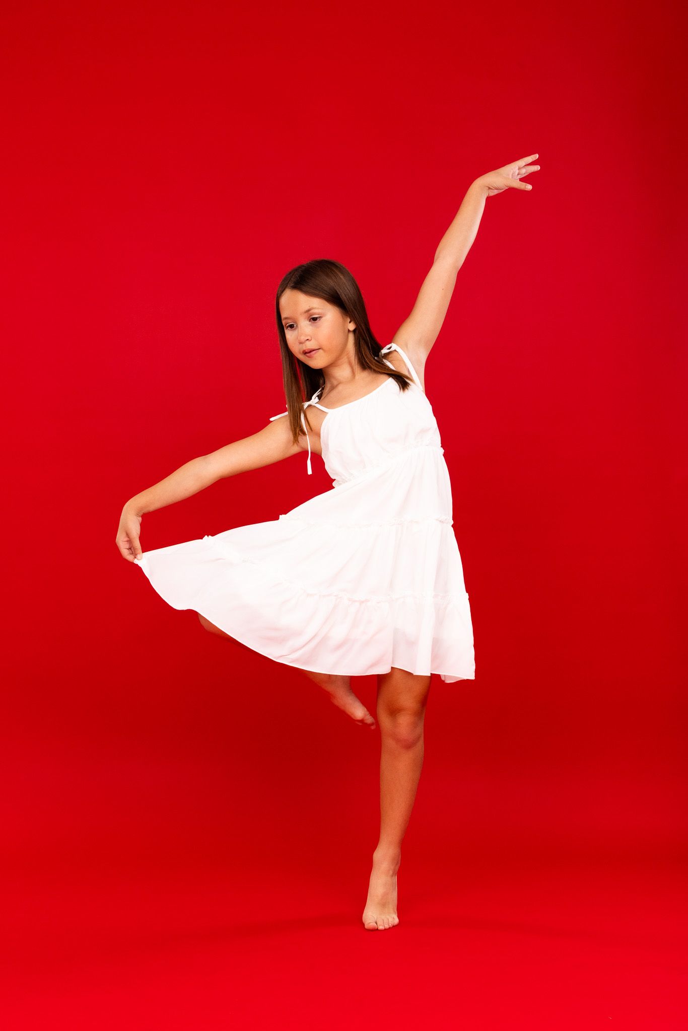 Graceful dancer in white dress performs elegant poses against vibrant red backdrop in artistic photo series.