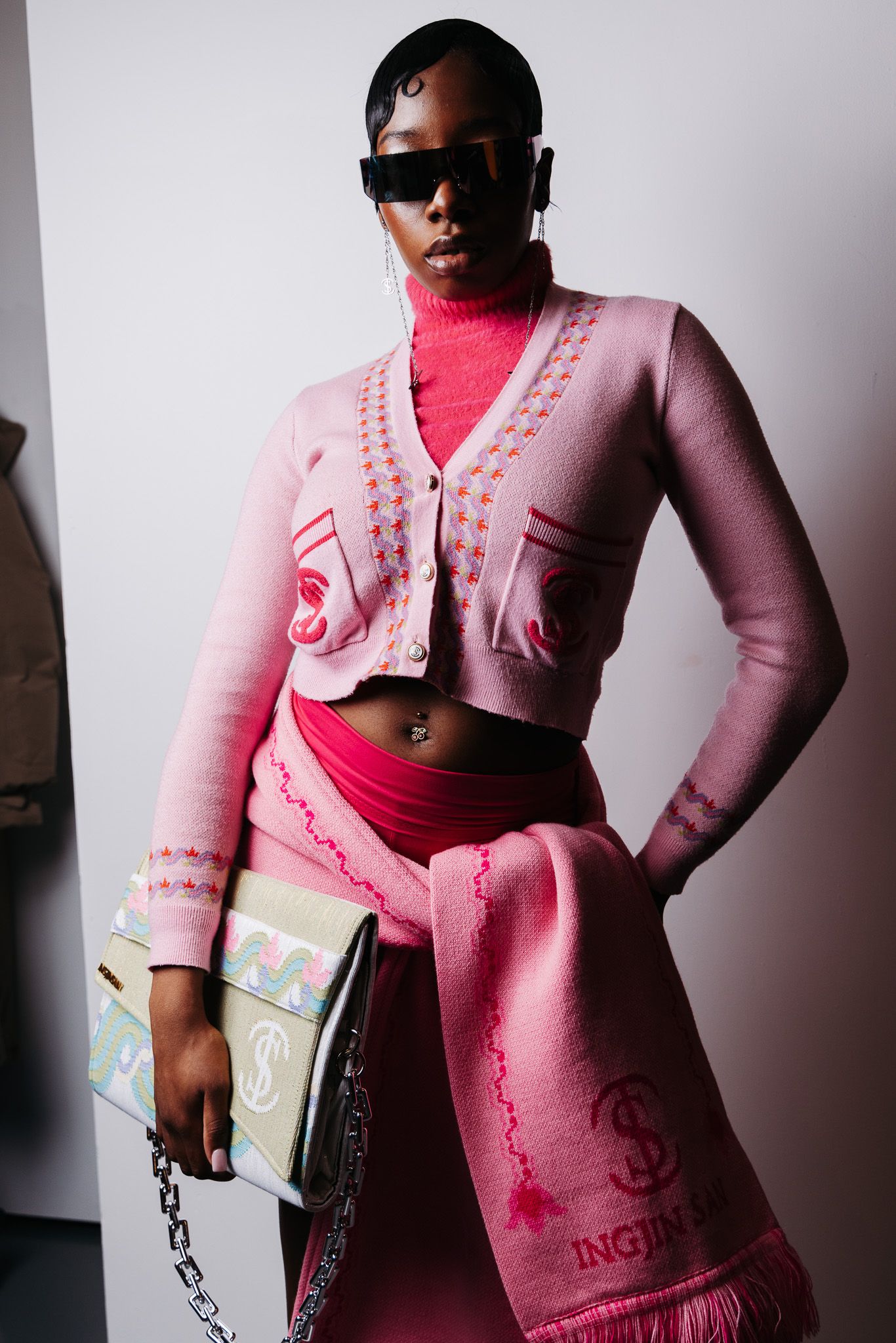 Fashion model wearing a pink cardigan and red top poses against white background in editorial style photoshoot.