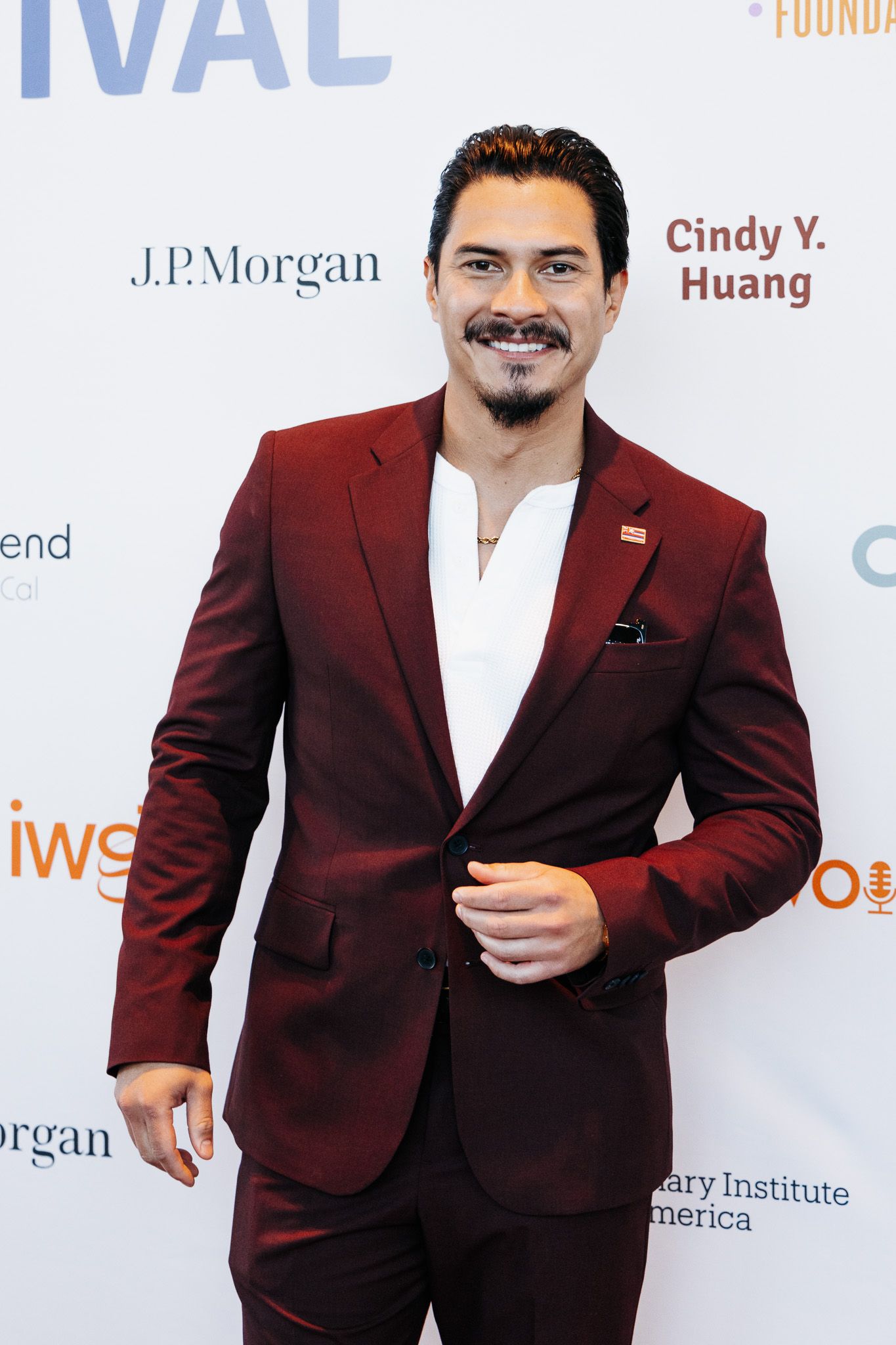 Person in burgundy suit jacket posing at a formal event backdrop.