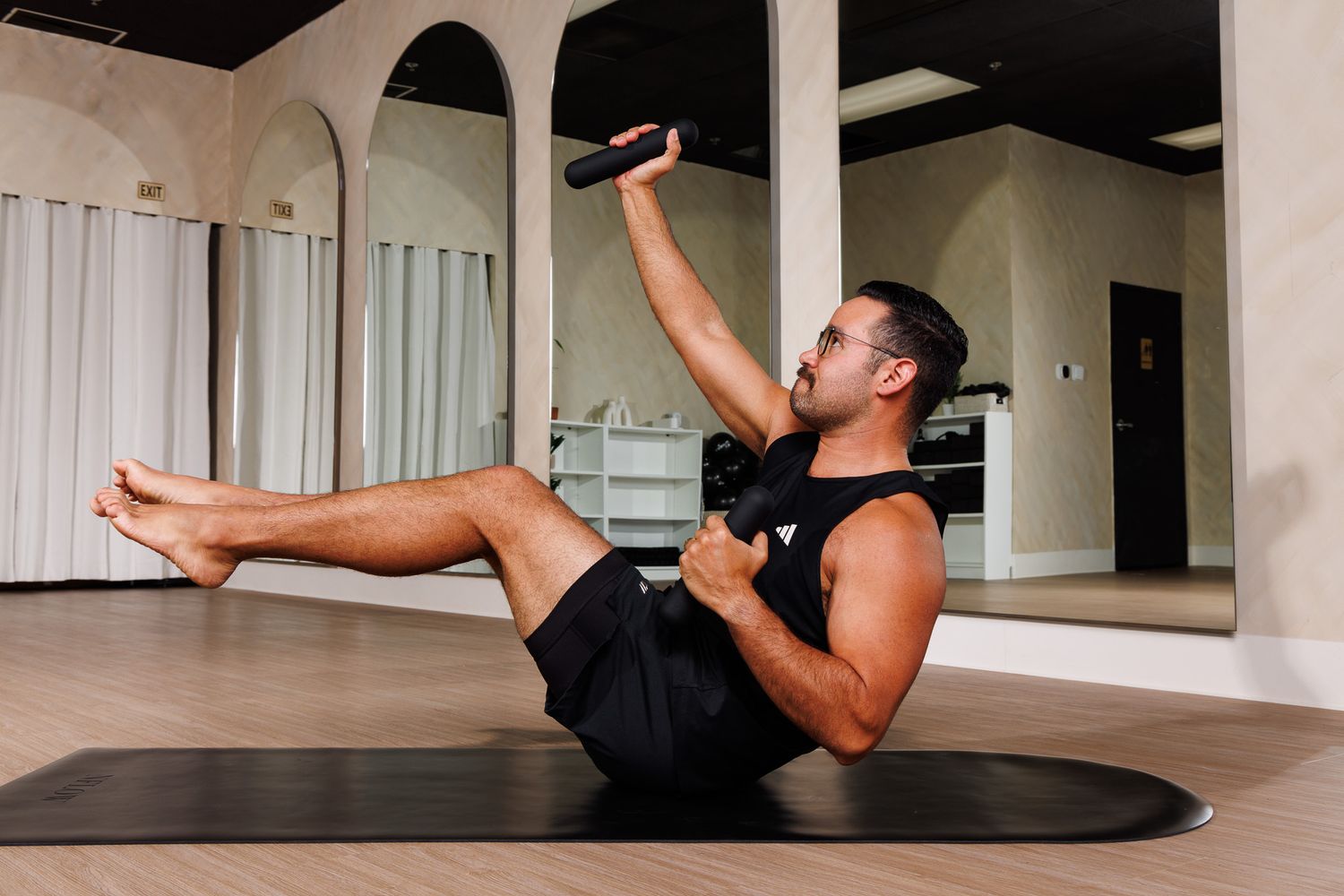 Athletic man in black doing core exercises with pilates ball on yoga mat in studio.