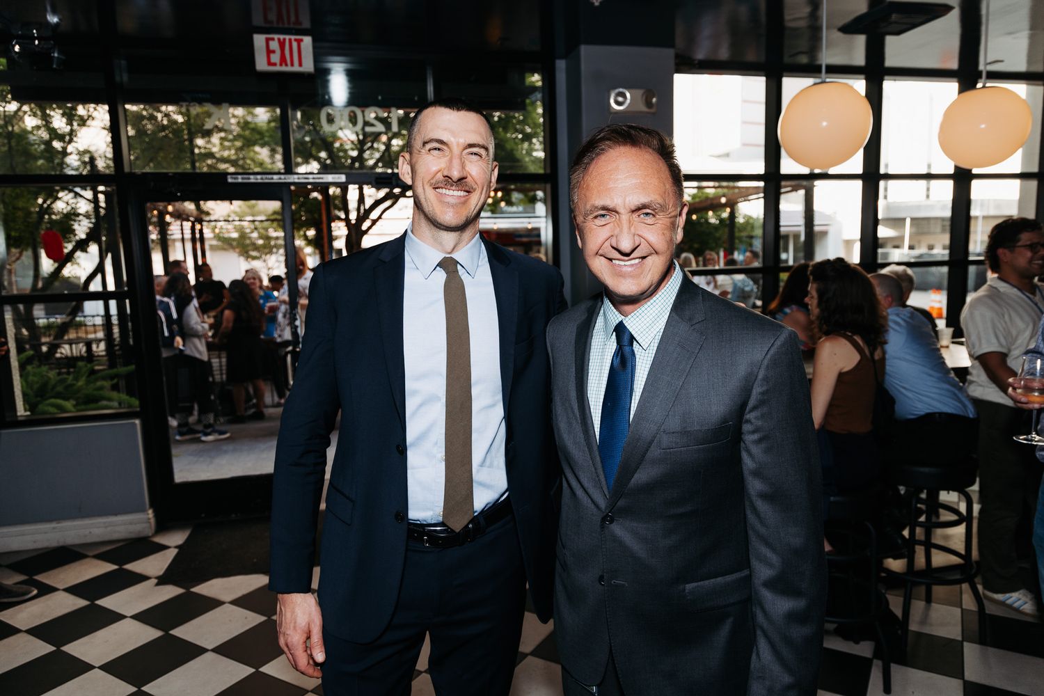 Several people in business attire gather and smile together at what appears to be a professional networking event.