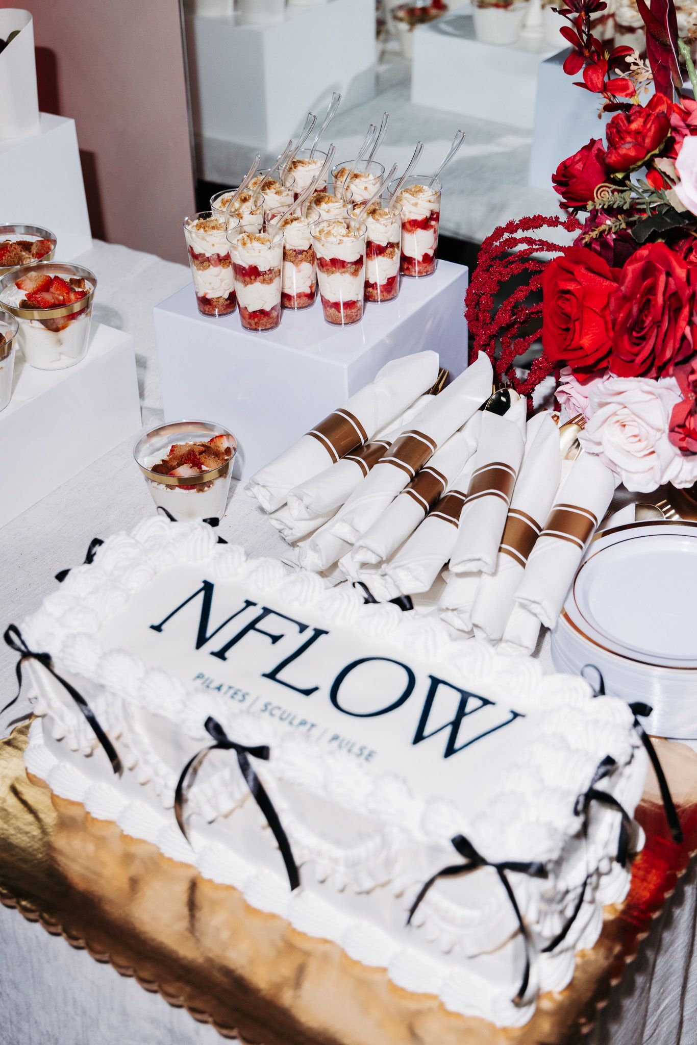 White decorated dessert table with NFLOW branding and red floral accents at an event.