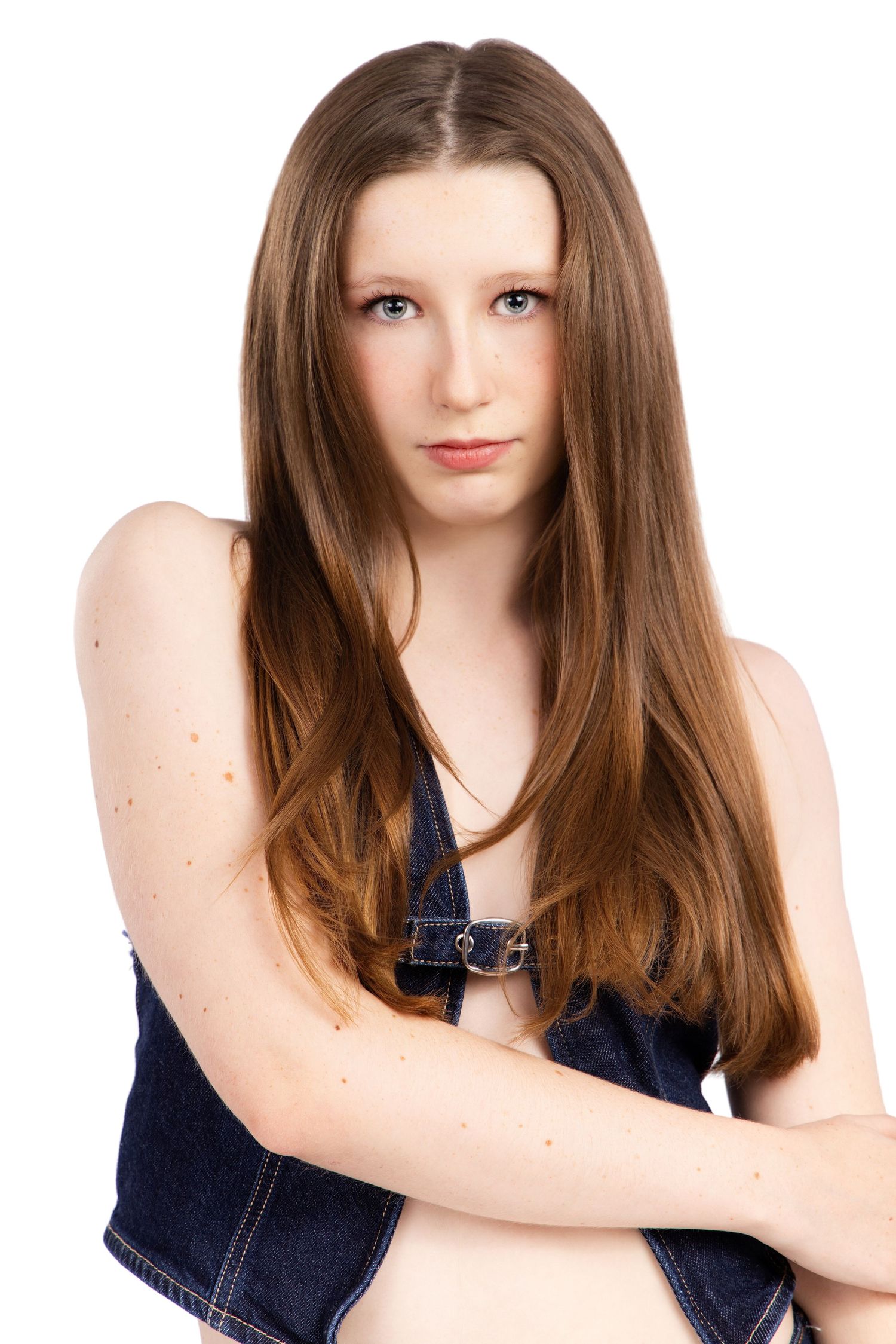 A young person with long brown hair poses in a dark denim vest against a white background.