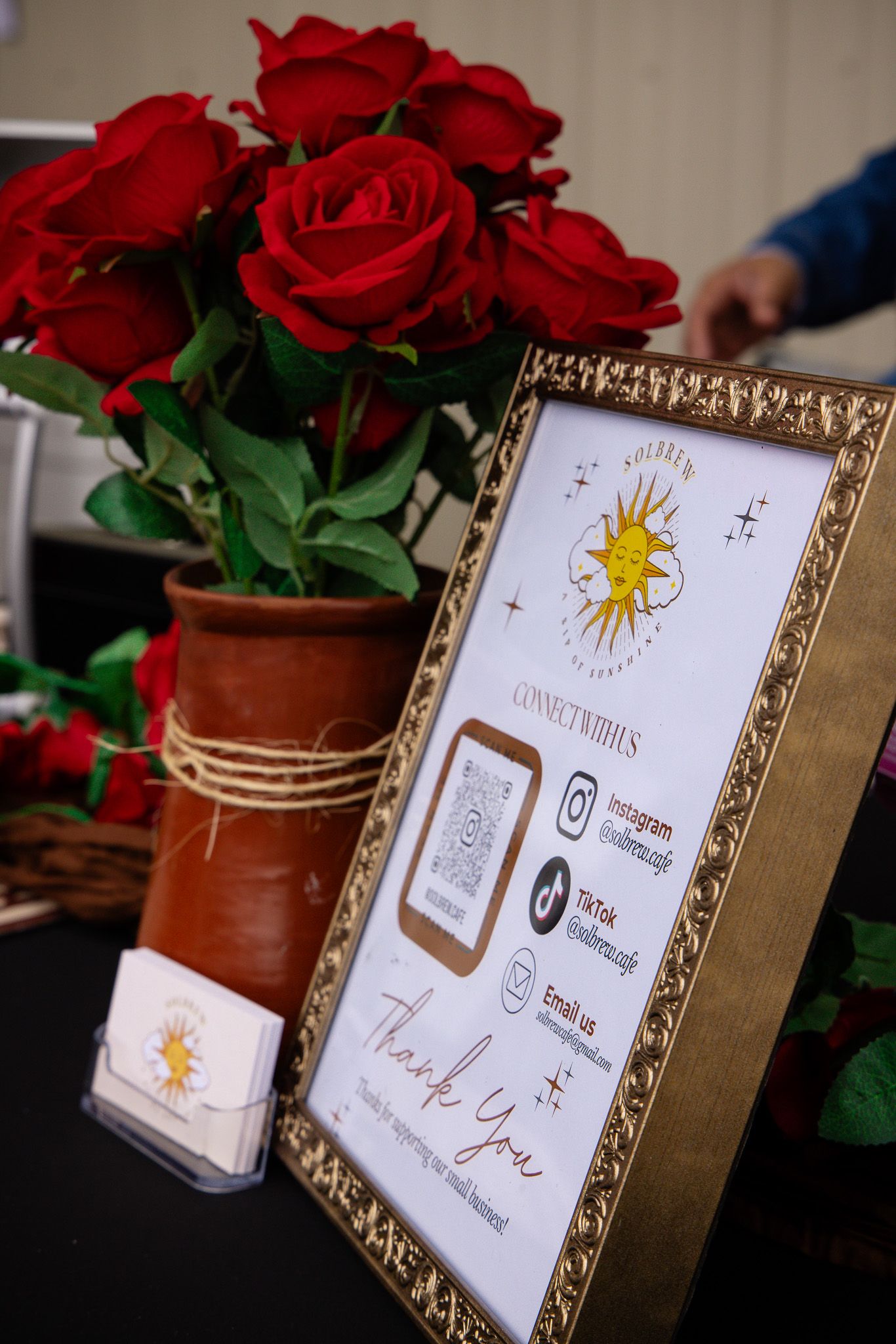 Framed event signage with sun illustrations displayed next to red roses in clay pots.