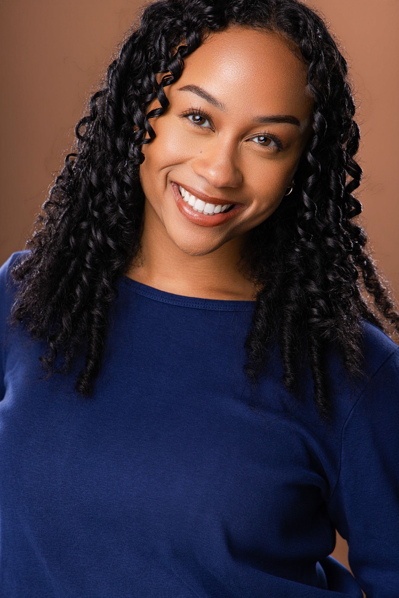 Smiling Black woman with curly braids wearing a blue top against a brown background.