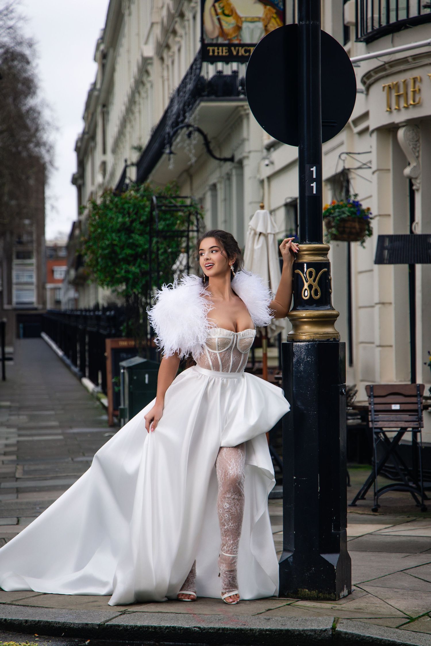 A bride in a flowing white dress poses gracefully on elegant city steps near classic architecture.