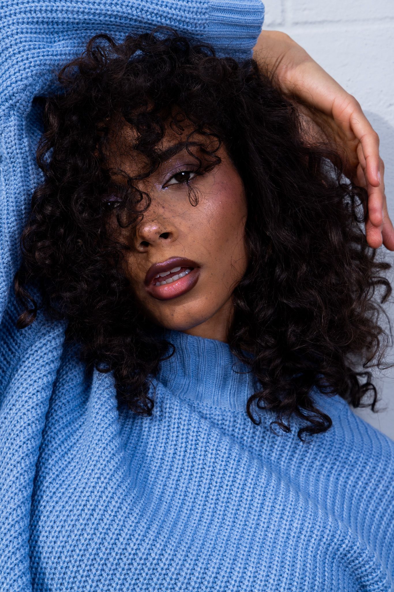 Close up portrait of model in blue sweater with curly hair and glamorous makeup.