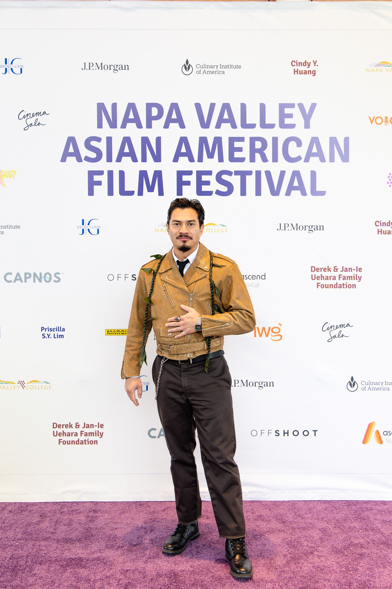 Person in brown vest poses on pink carpet at Napa Valley Asian American Film Festival.