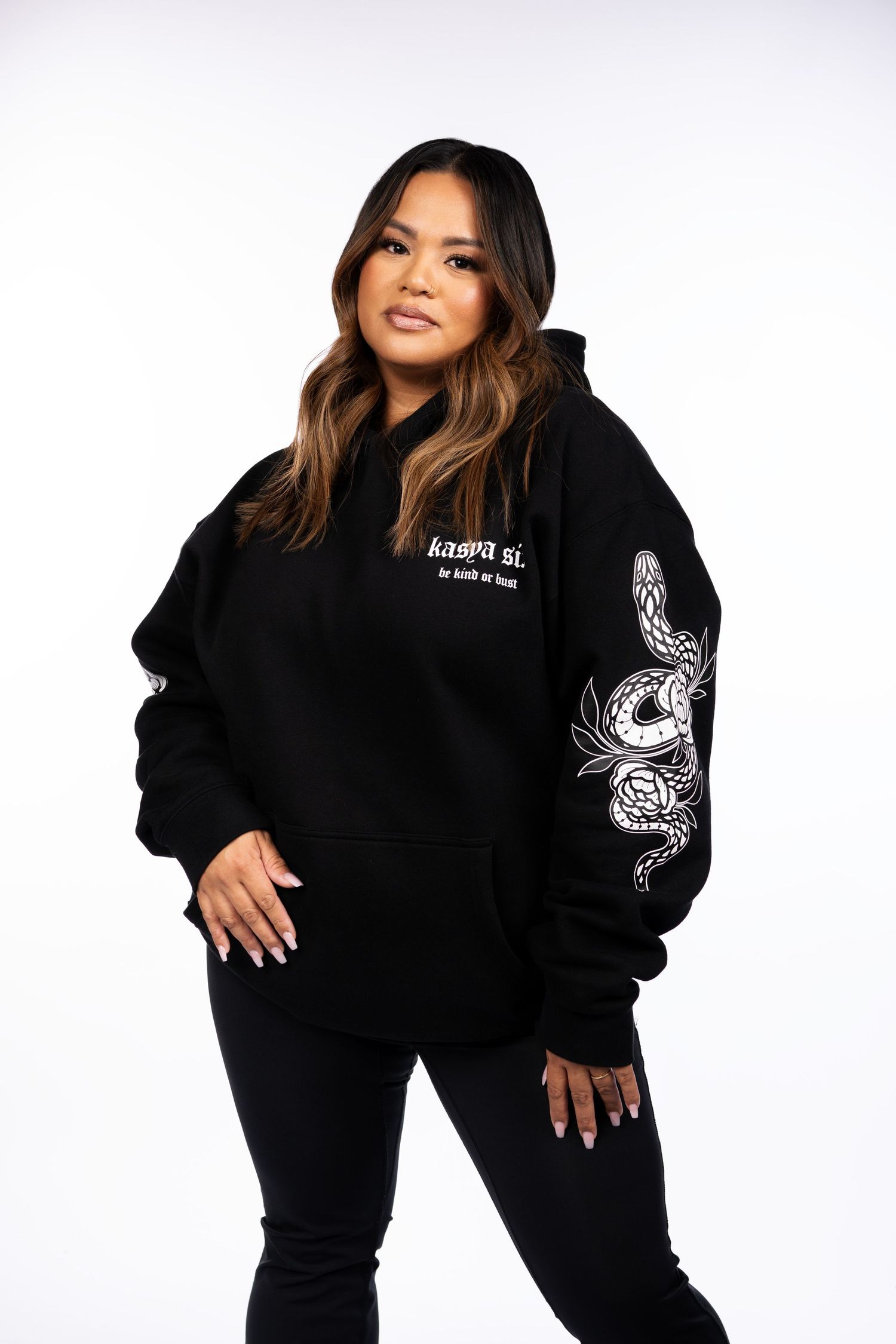 Woman posing in black oversized hoodie with snake graphic and text print, paired with black pants.